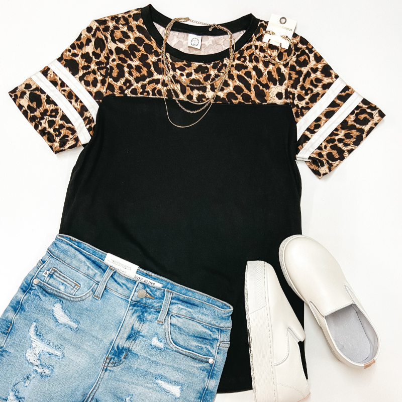 A black top with a leopard print short sleeve upper. Pictured with denim shorts, white sneakers, and gold jewelry.