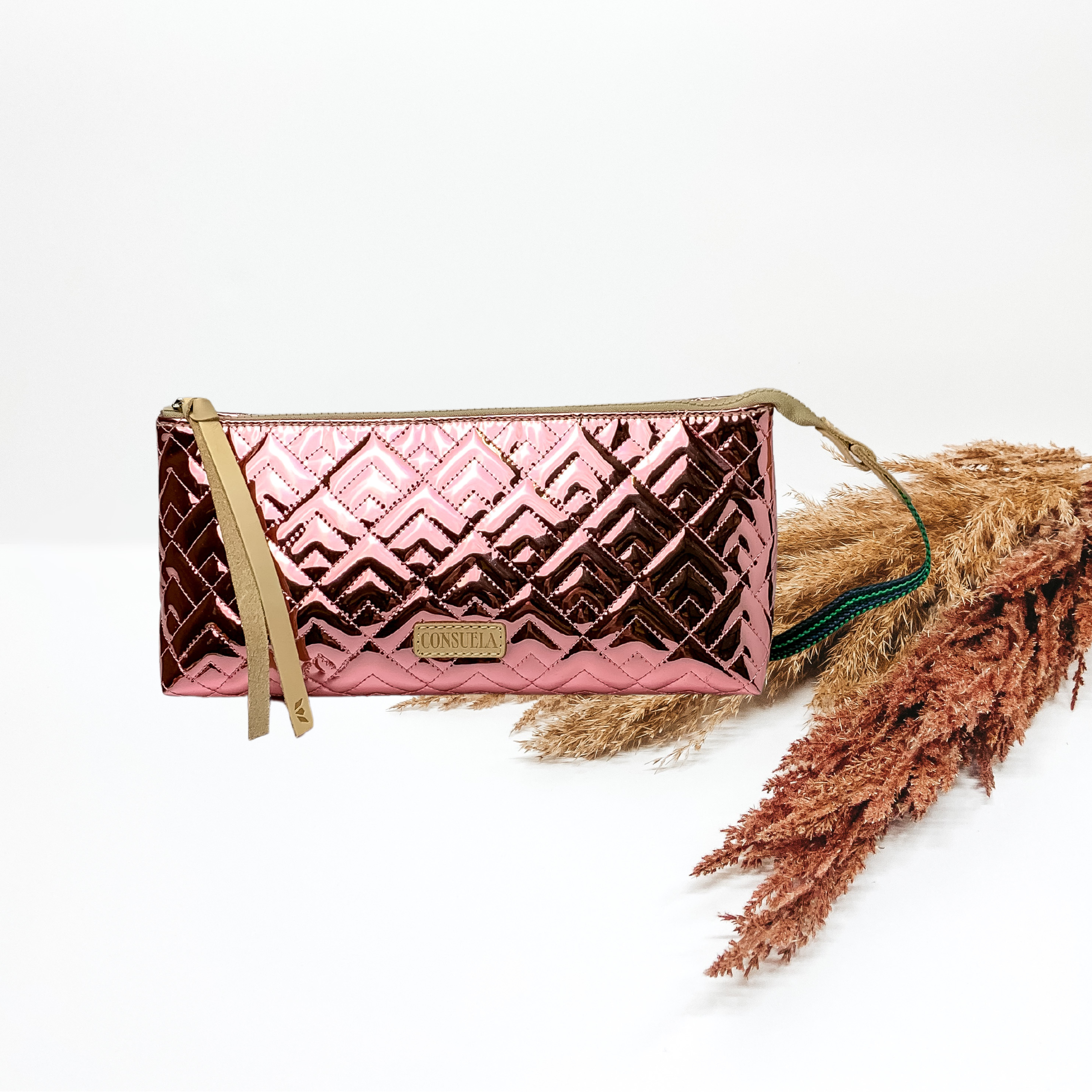 In the middle of the picture is a tool bag in a quilted metallic pink pattern. Bag is on a solid white background with pompas grass to the right of the bag. 