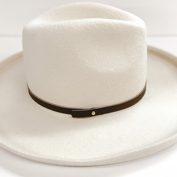 A thin leather hat band that is dark brown. The hat band has a gold pin. Pictured on ivory felt hat.
