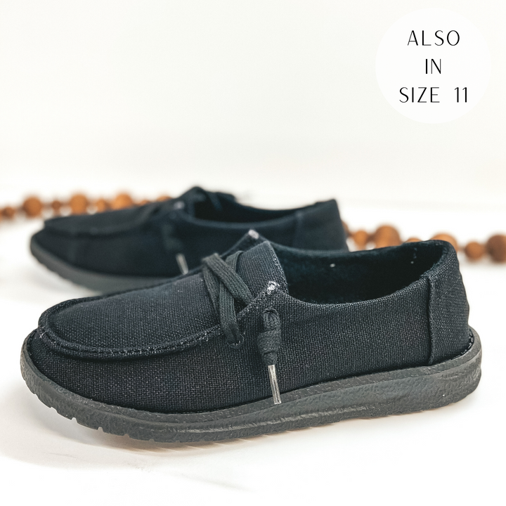 A pair of solid black lace up loafers pictured on a white background with brown beads.