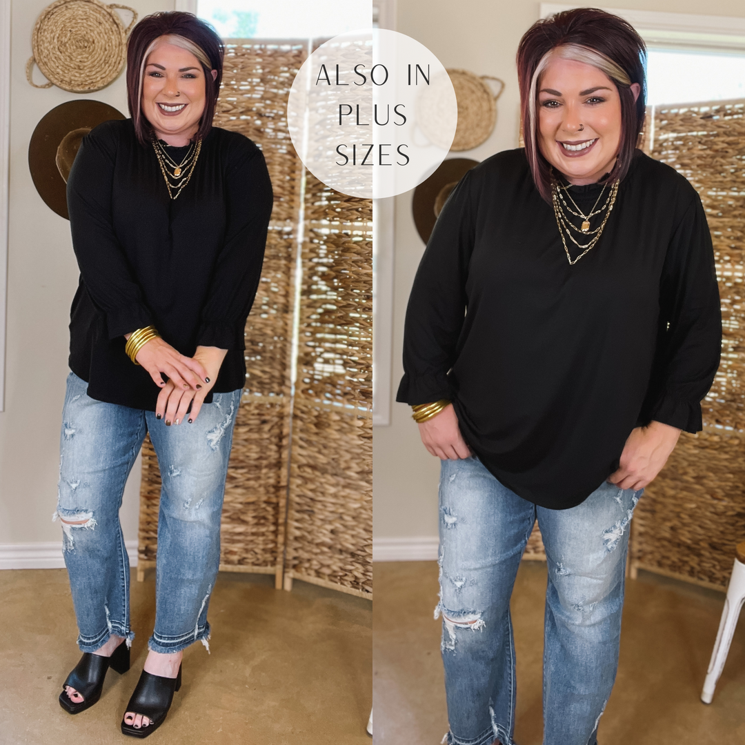 Model is wearing a long sleeve black top with a mock neckline. Model has it paired with distressed jeans, black heels, and gold jewelry.