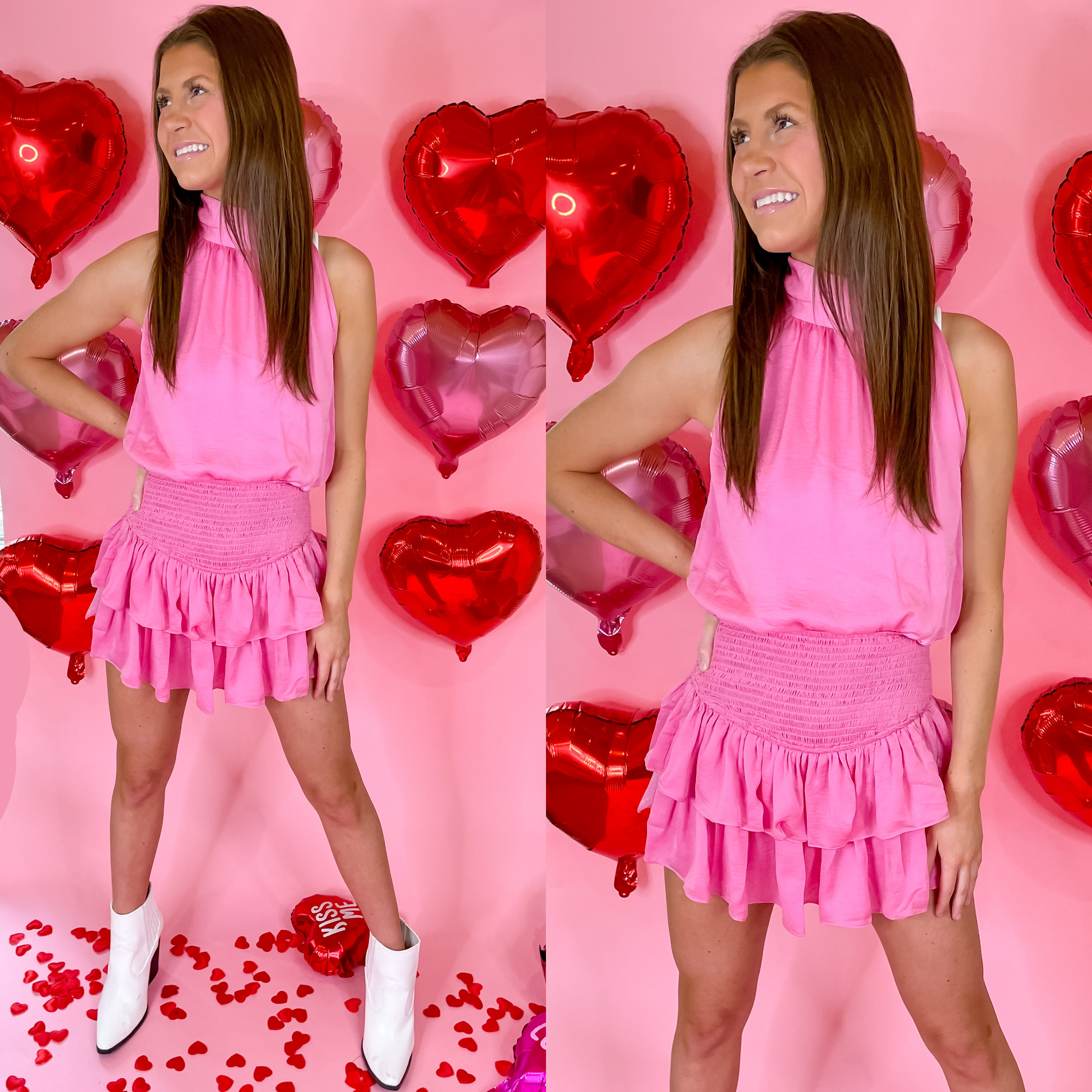 Model is wearing a romper with a smocked waist and a ruffle skirt in pink. Model has this romper paired with white booties. Background is light pink with red heart balloons. 