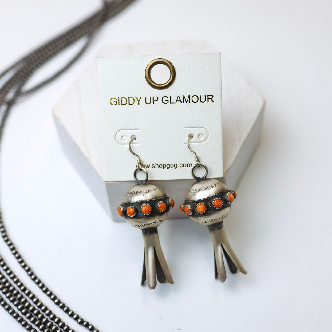 Monica Smith Navajo Handmade Sterling Silver Blossom Earrings with Orange Spiny Oyster are centered in the middle of the picture with navajo pearls laid to the left of the earrings. All on a white background. 