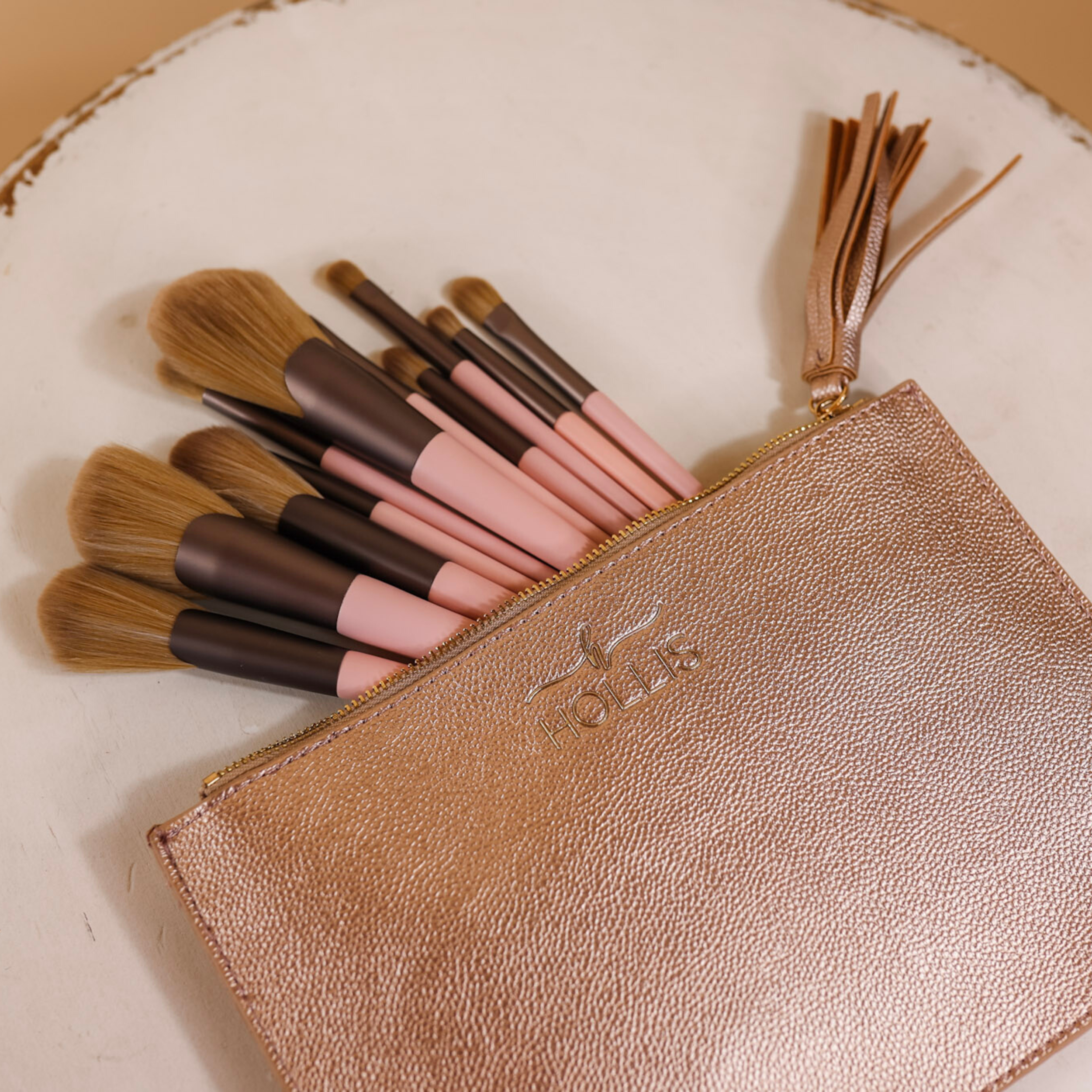 A brush pouch is laid in the middle of the picture in rose gold. Laying inside the pouch are 11 different sized makeup brushes in pink and brown. Background is white. 