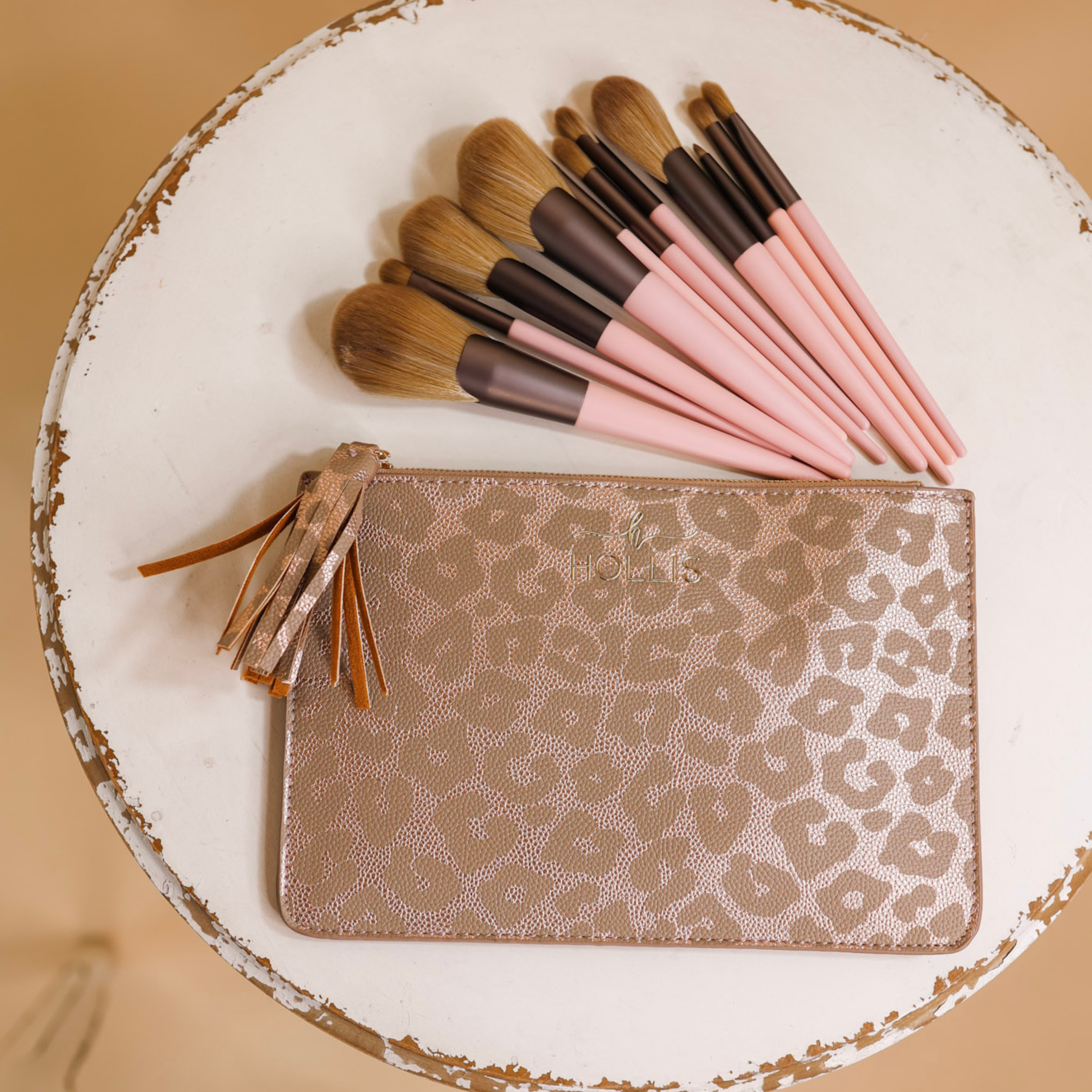 A leopard pouch is sitting in the middle of the picture with 11 different sized makeup brushes in pink and brown above the pouch. Background is white and tan. 