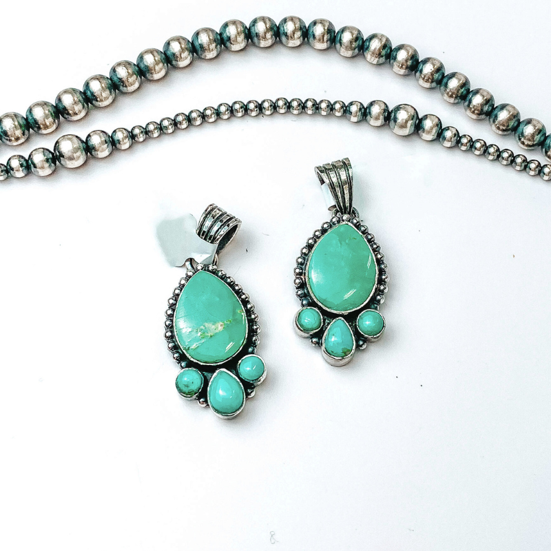 Centered in the picture is teardrop pendants with three accent stones at the bottom. Navajo pearls are laid above the pendants, all on a white background. 