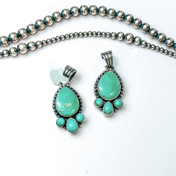 Centered in the picture is teardrop pendants with three accent stones at the bottom. Navajo pearls are laid above the pendants, all on a white background. 