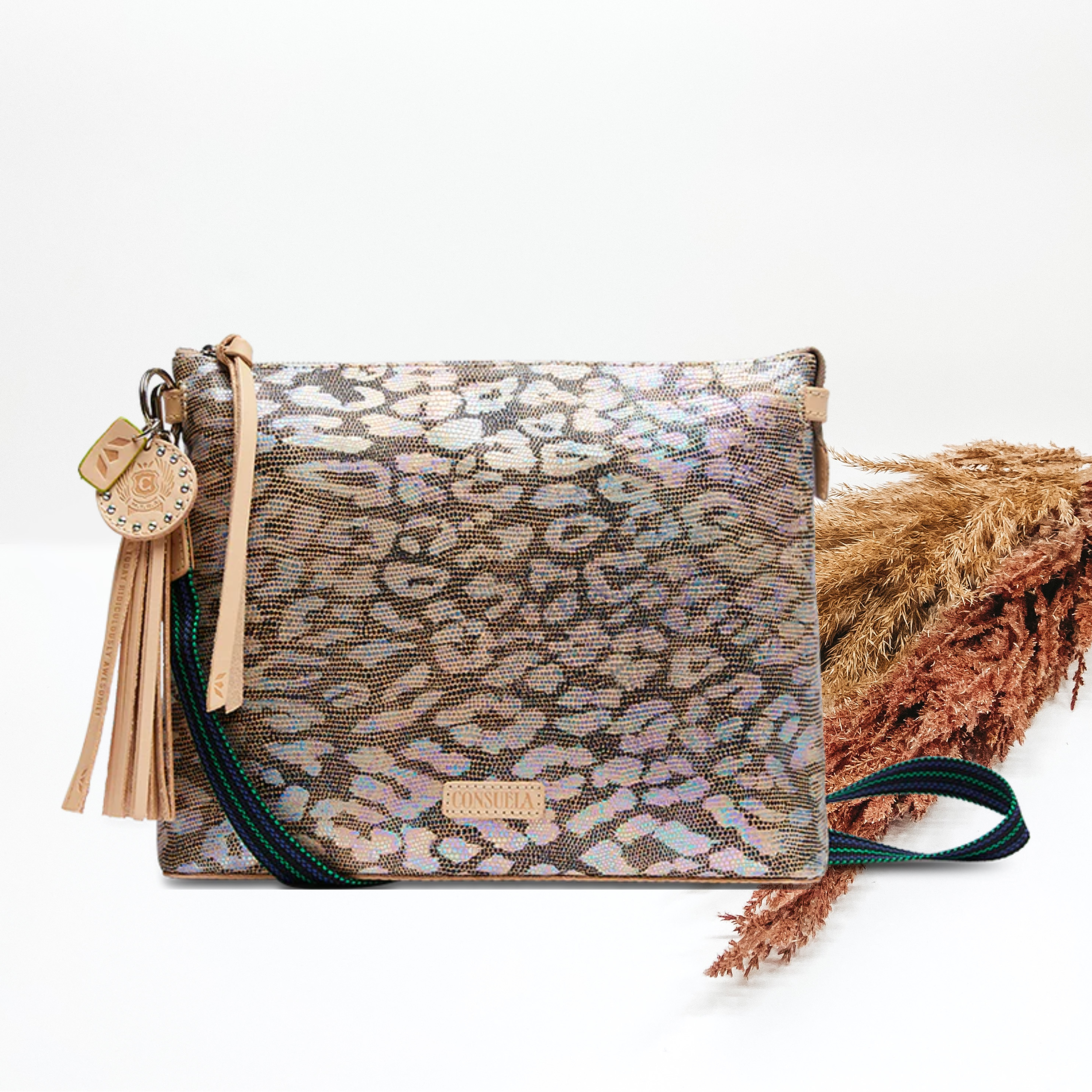 Centered in the picture is a crossbody bag in a rainbow leopard print. The background is pompas grass and solid white. 