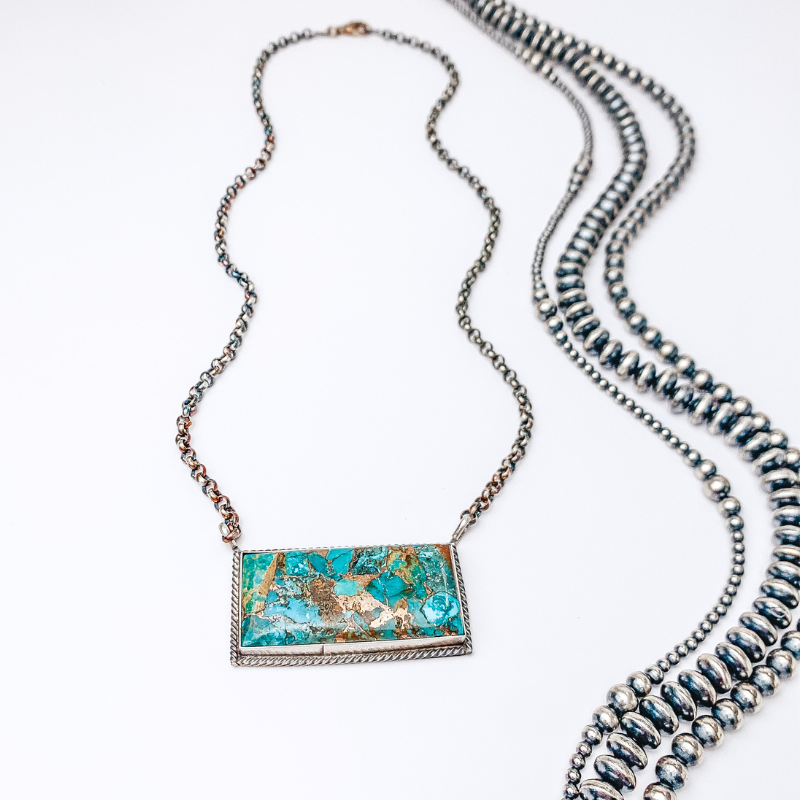 Centered in the picture is a sterling silver necklace with a large turquoise bar pendant. Background is solid white. 