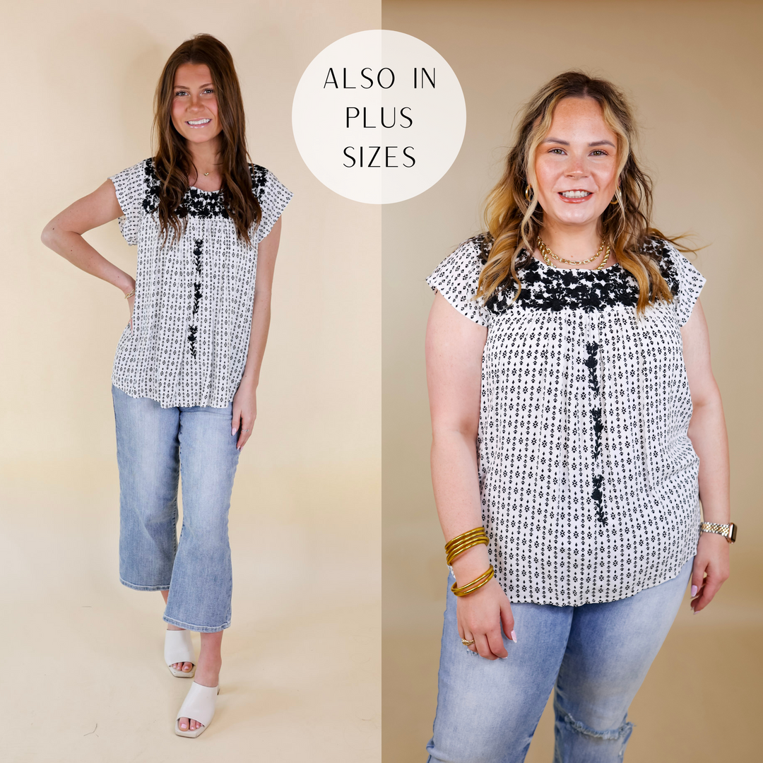 Model is wearing a black and white tribal print shirt with black floral embroidery around the upper. Model has it paired with light wash jeans, ivory heels, and gold jewelry.