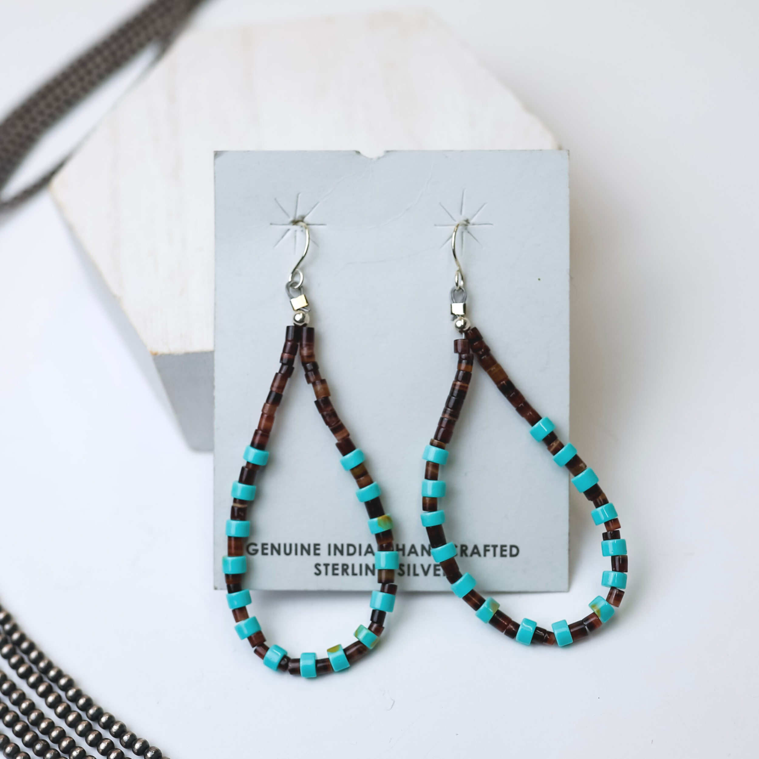 Corraine Smith Navajo Handmade Turquoise Bead Teardrop Earrings bare centered in the middle of the picture with navajo pearls laid on the bottom left corner. All on a white background. 