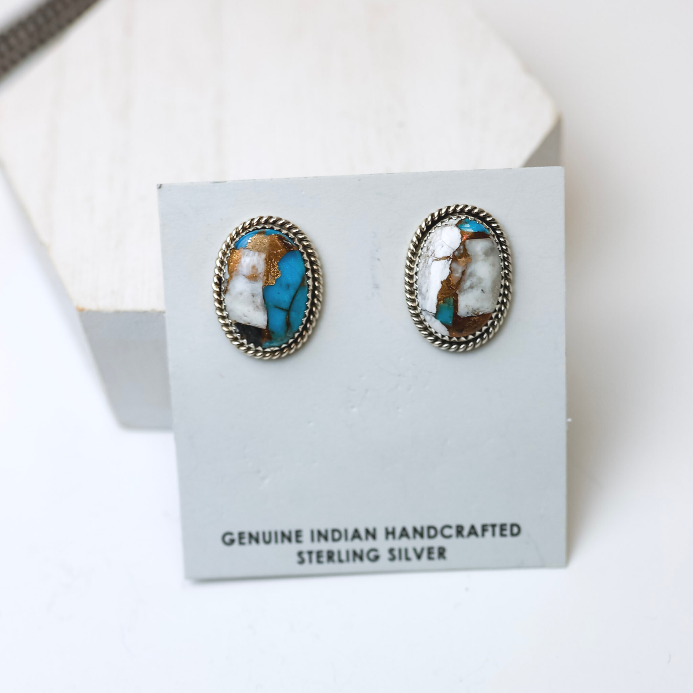 Navajo Handmade Sterling Silver and Remix White Buffalo Turquoise Oval Stud Earrings are centered in the picture, with navajo pearls in the top left corner. All is on a white background. 