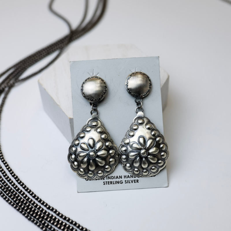 Tim Yazzie Navajo Handmade Genuine Sterling Silver Post Back Dangle Earrings with Flower Teardrop are in the center of the picture, with navajo pearls to the left of the earrings. All on a white background. 