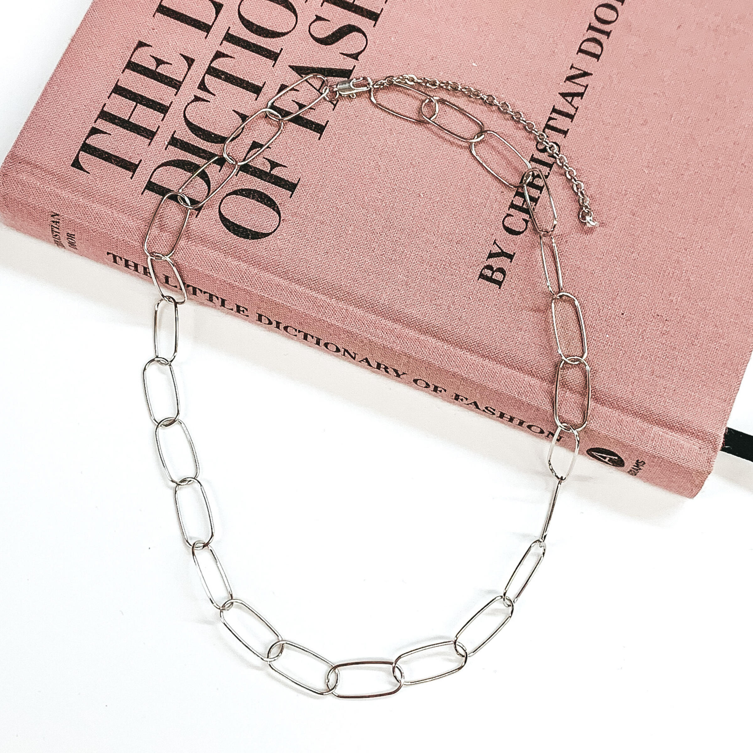Thin, paperclip chain in silver. This necklace is pictured laying partially on a mauve colored book on a white background. 