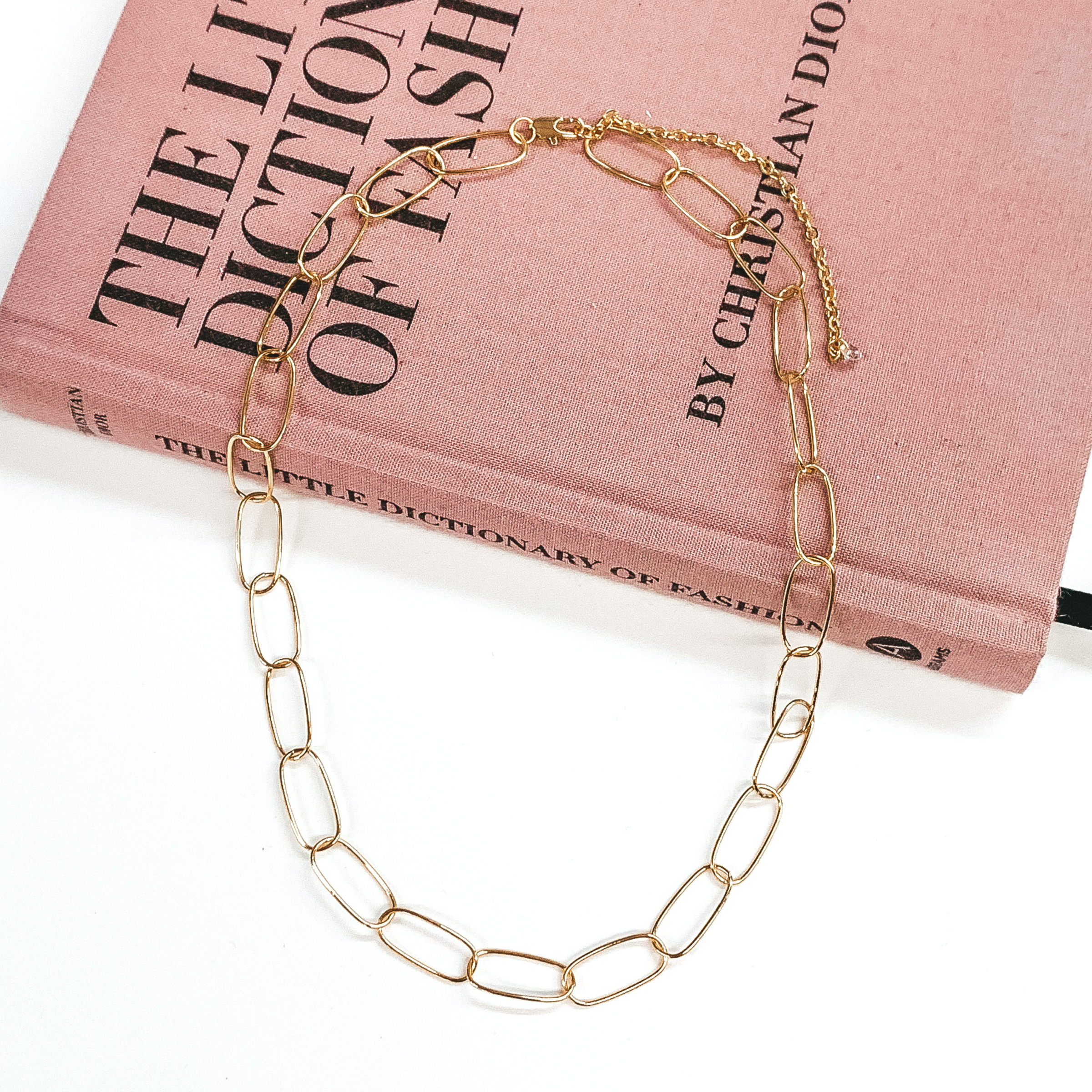 Thin, paperclip chain in gold. This necklace is pictured laying partially on a mauve colored book on a white background. 