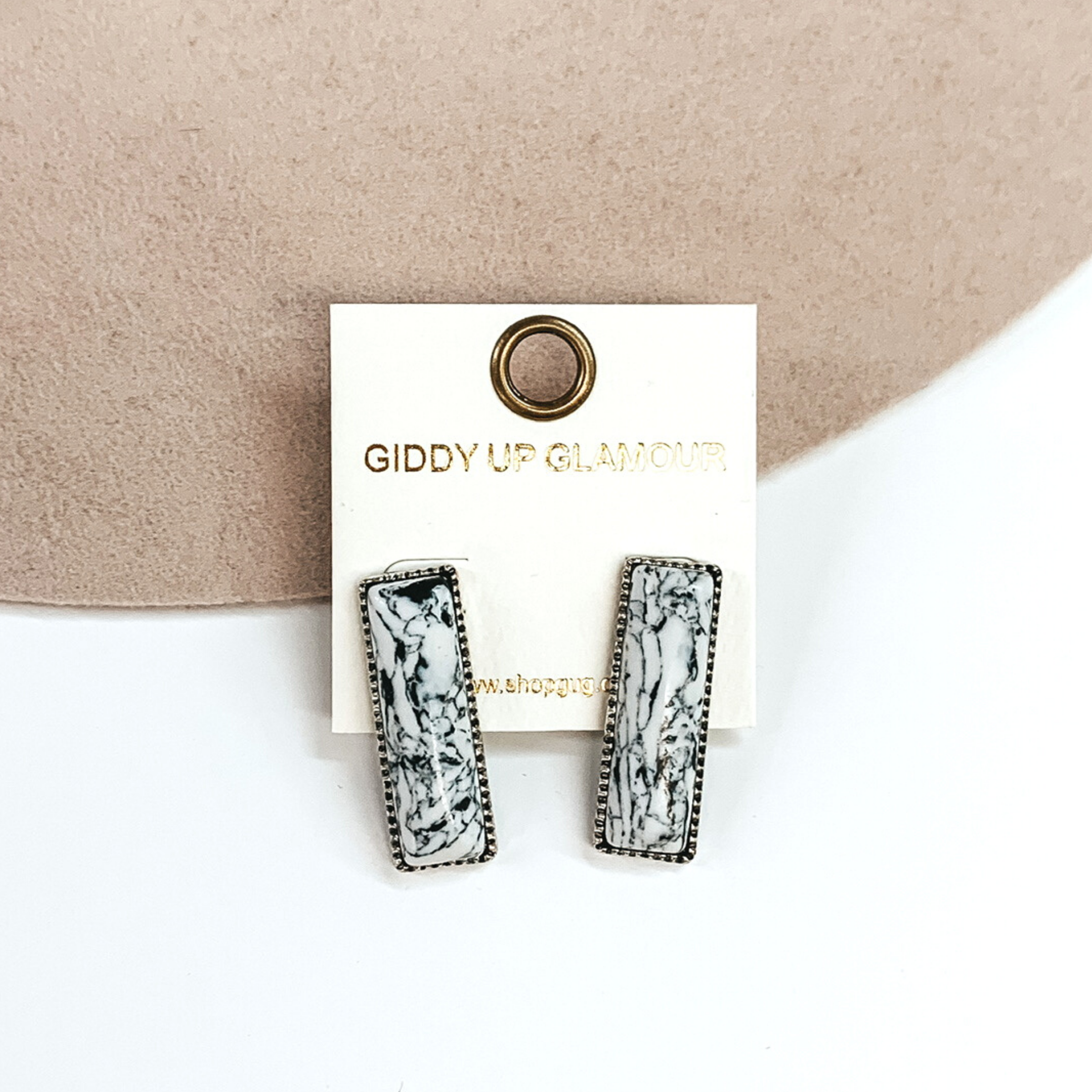 Silver rectangle earrings with a white rectangle stone. These earrings are pictured on a white and beige background. 