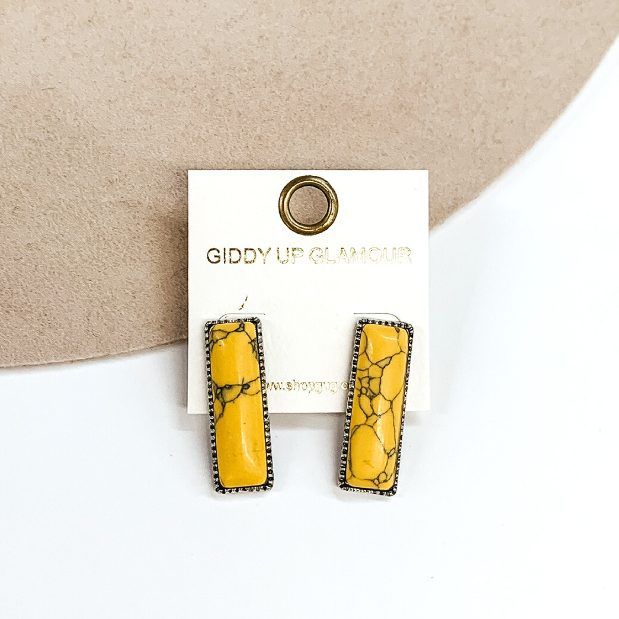 Silver rectangle earrings with a yellow rectangle stone. These earrings are pictured on a white and beige background. 