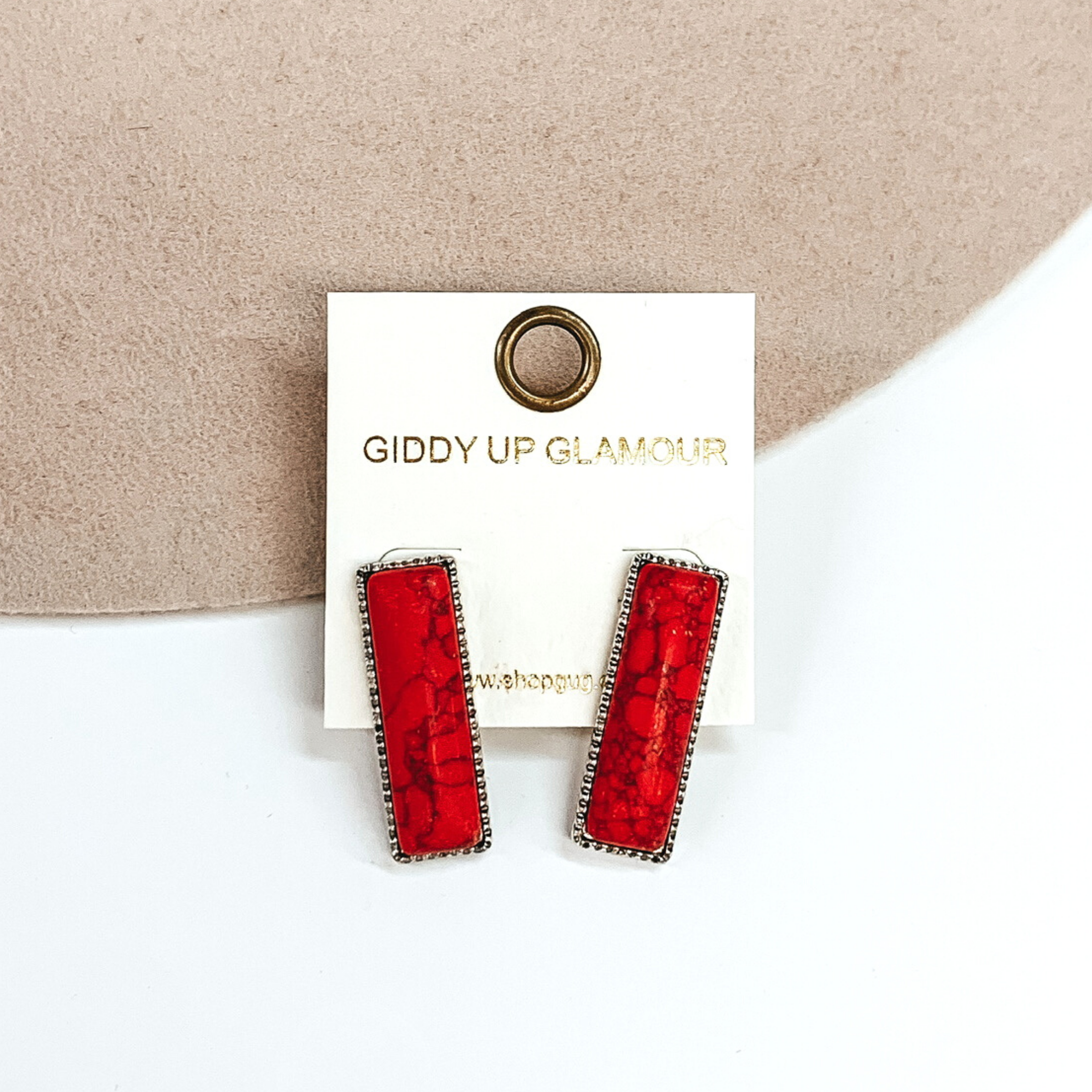 Silver rectangle earrings with a red rectangle stone. These earrings are pictured on a white and beige background. 
