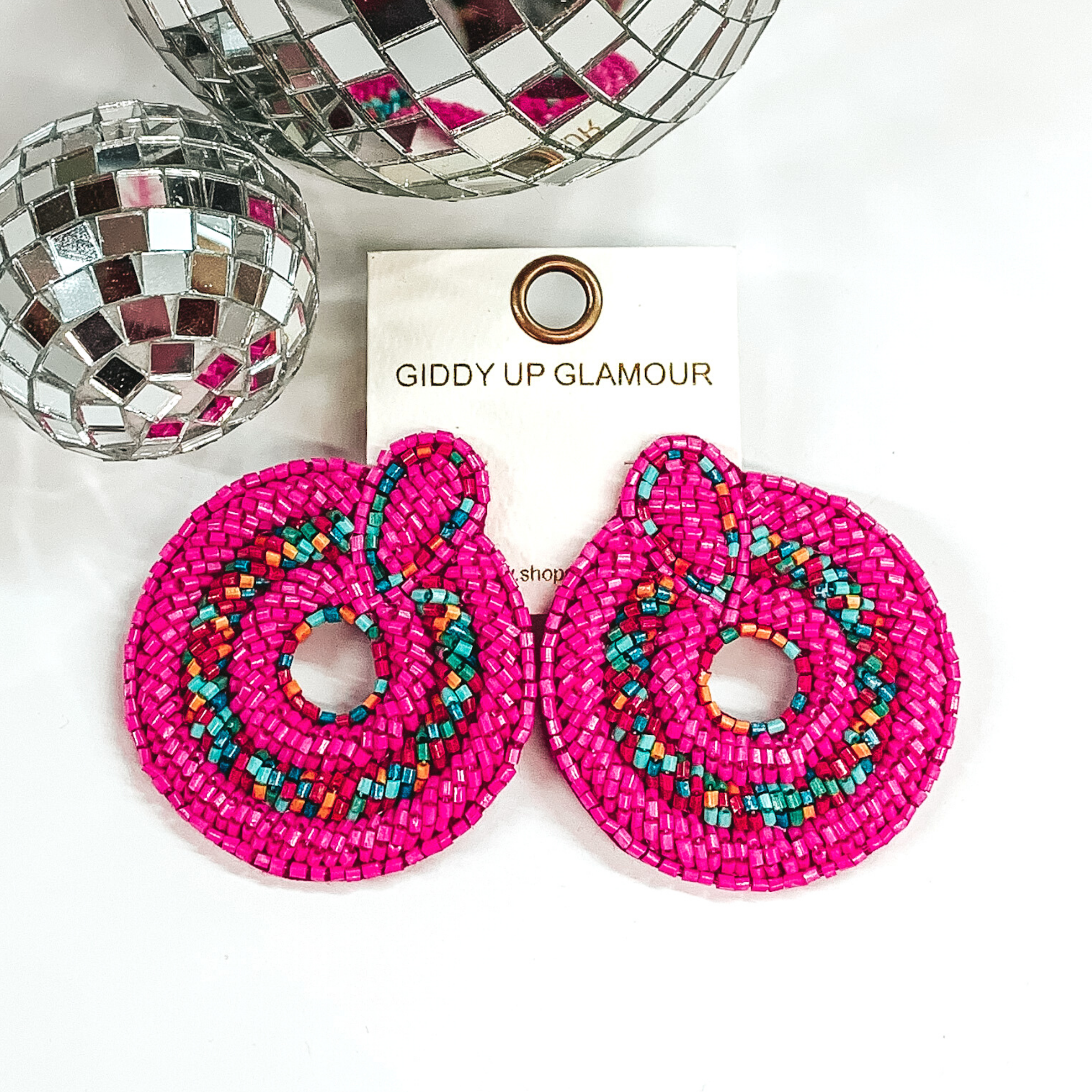 Fuchsia circle beaded earrings with a multicolored stripe in the middle of the circle and an open small circle in the middle of the earrings. These earrings are pictured on a white background with disco balls in the top left corner. 