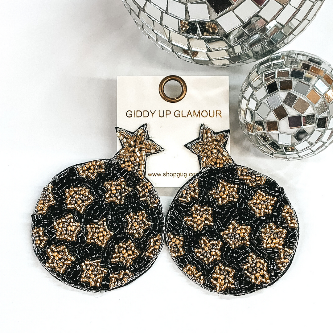 Black circle beaded circles with a gold beaded star at the top. The circle has gold beaded star design. These earrings are pictured on a white background with disco balls at the top right corner of the picture. 