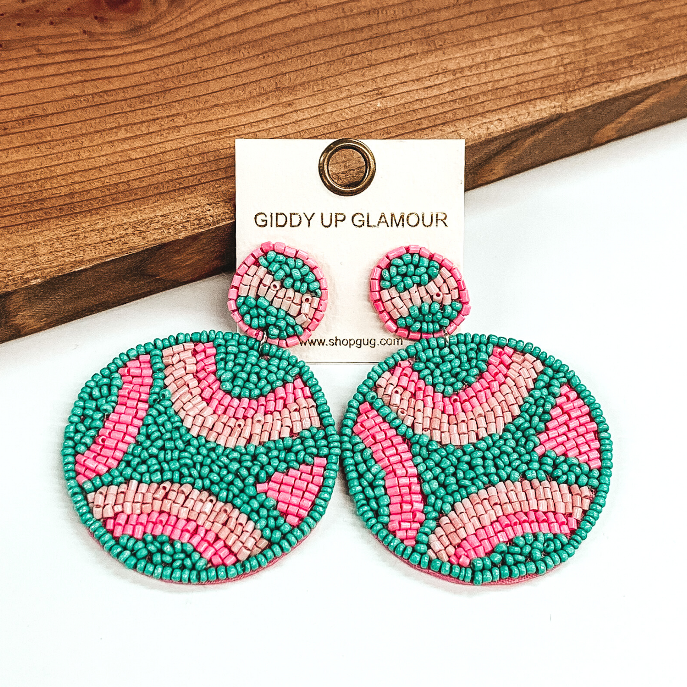 Circle beaded studs with a beaded hanging circle. Both include a turquoise, pink, and light pink design. These earrings are pictured in front of dark colored wood on a white background. 