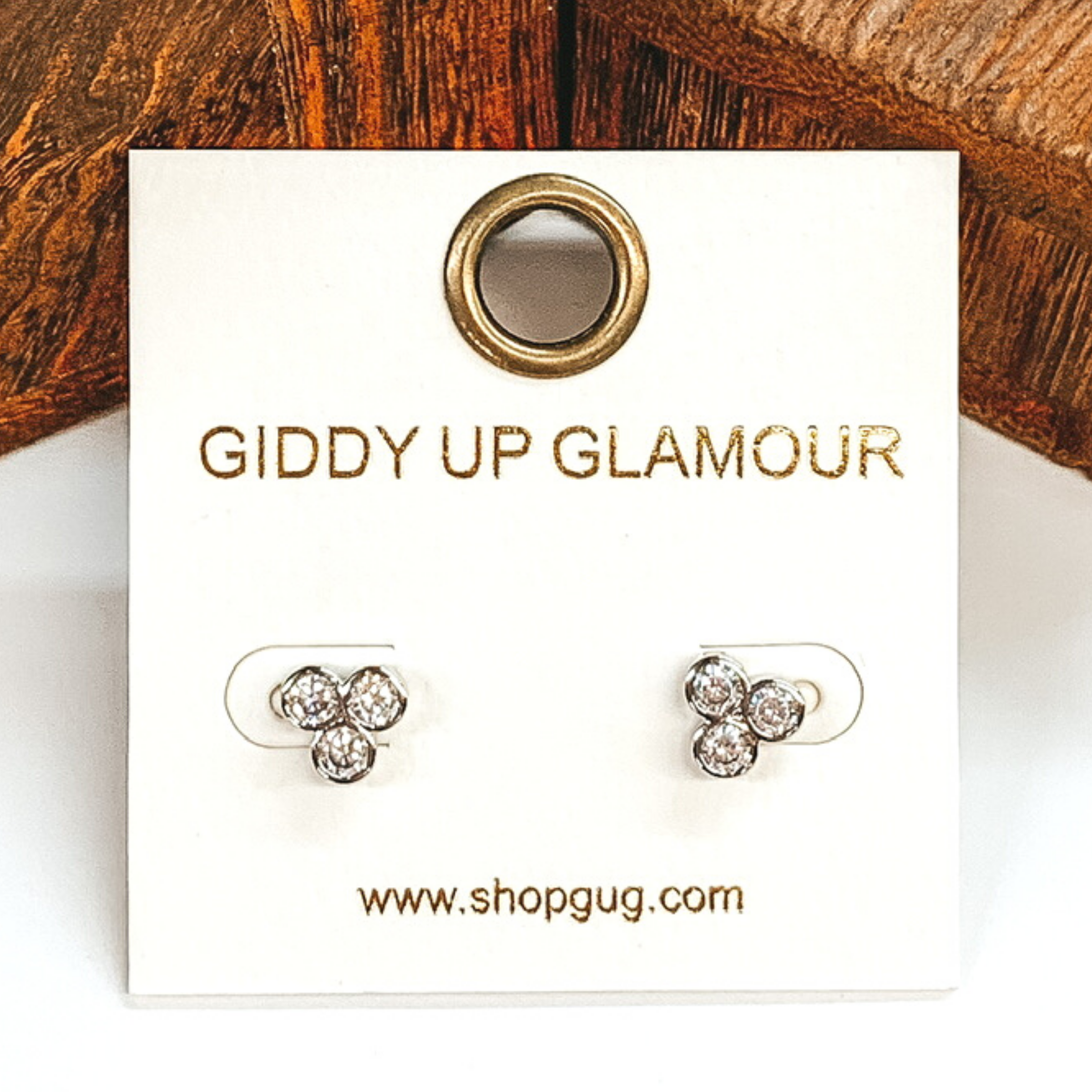 Small, silver circle cluster crystal stud earrings. These earrings are pictured on a white earrings card on a white and brown background.