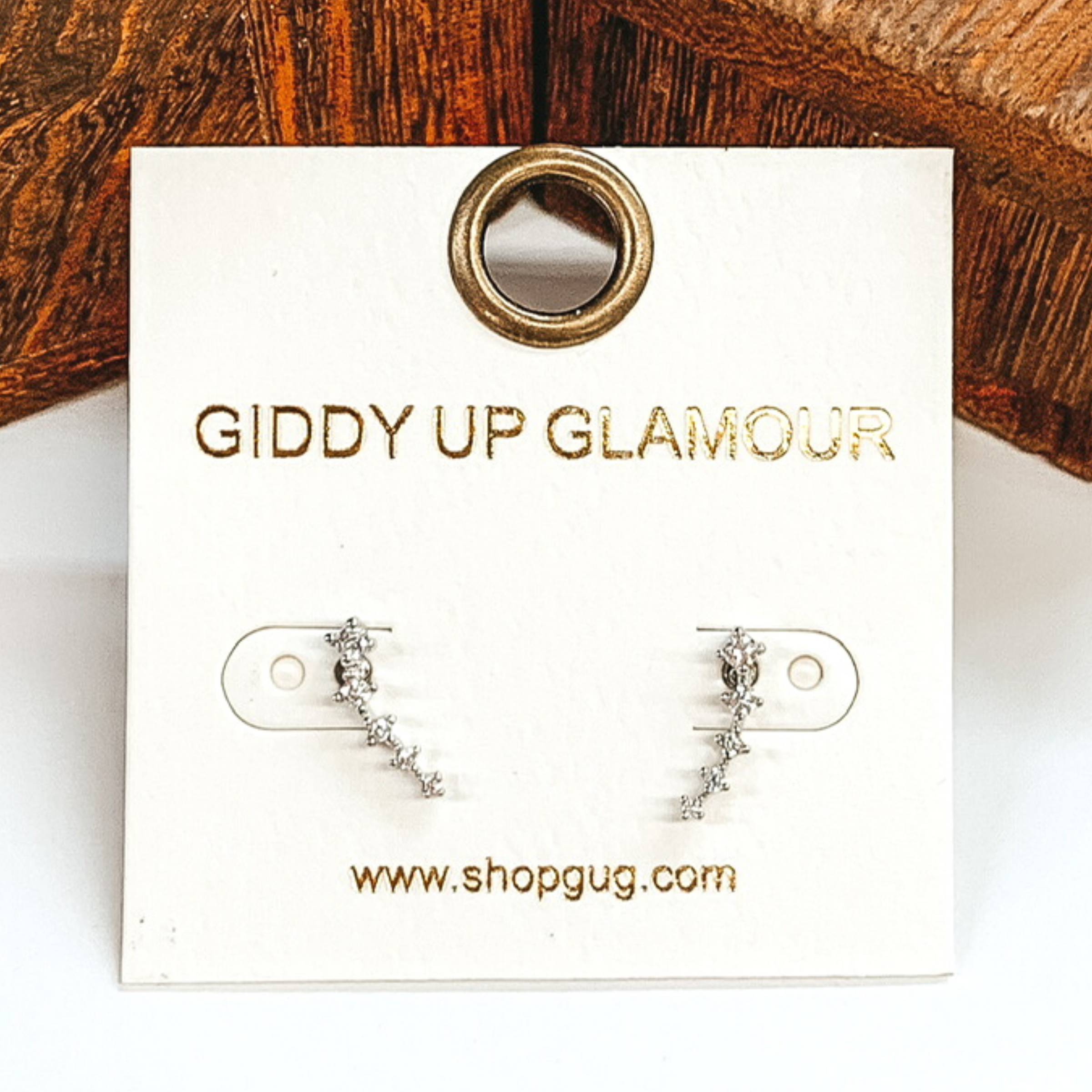Silver and clear crystals ear climbing stud earrings. These earrings are pictured on a white and brown background. 