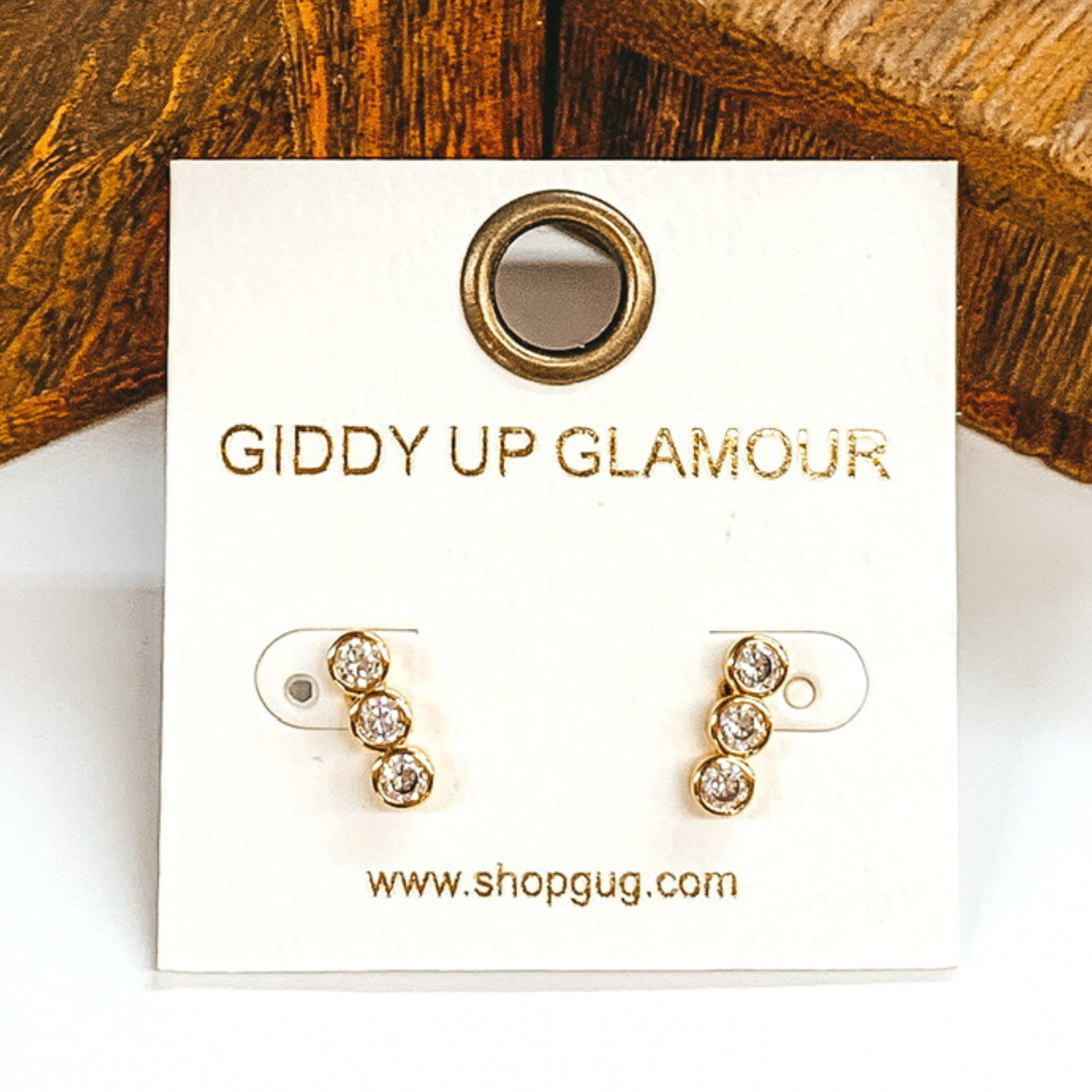 Small, silver circle stacked stud earrings with clear crystals. These earrings are pictured on a white earrings card on a white and brown background.