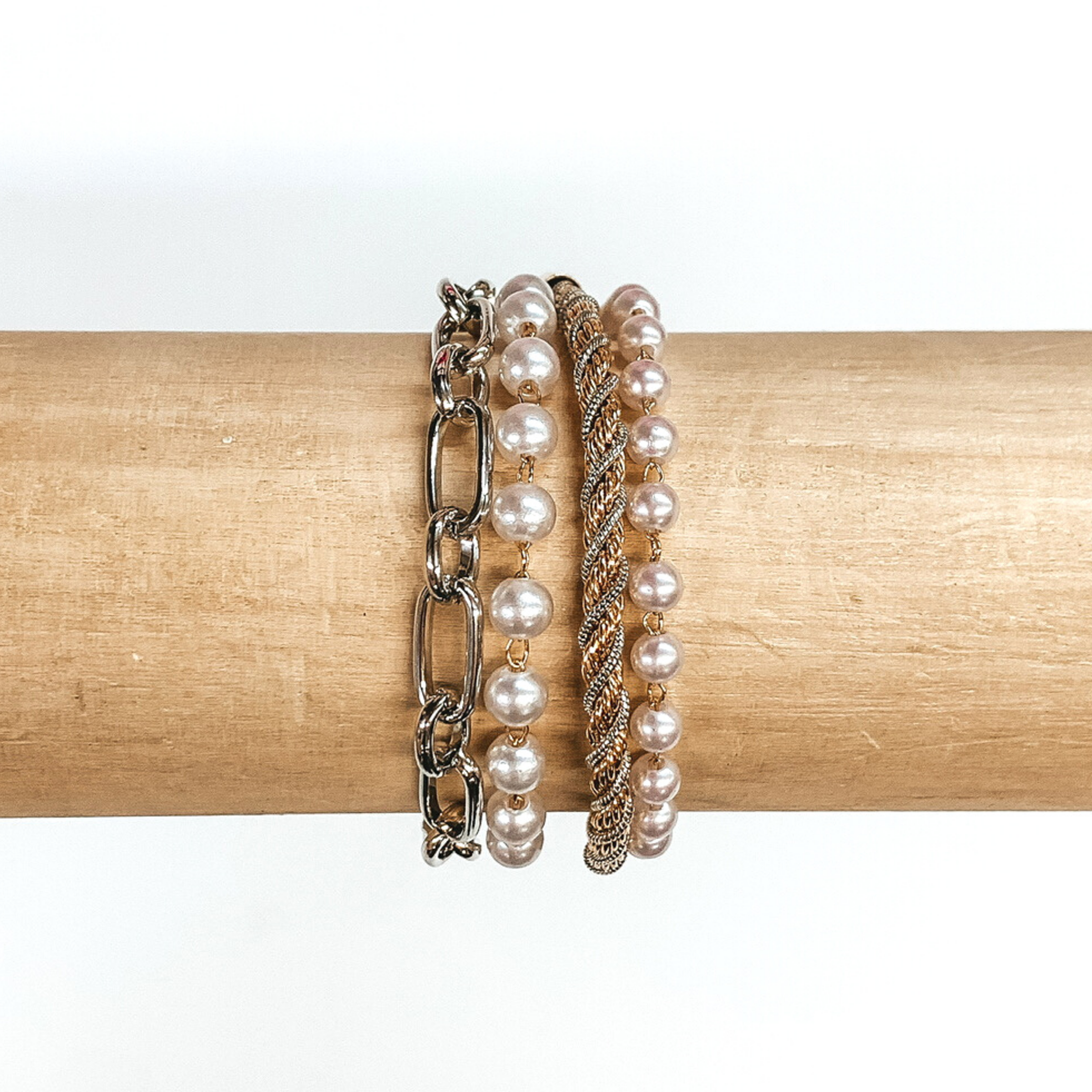 Four stranded bracelet pictured on a wood bracelet holder on a white background. This bracelet has a silver chained strand, two pearl linked with gold circles strand, and a gold and silver rope chain strand. 