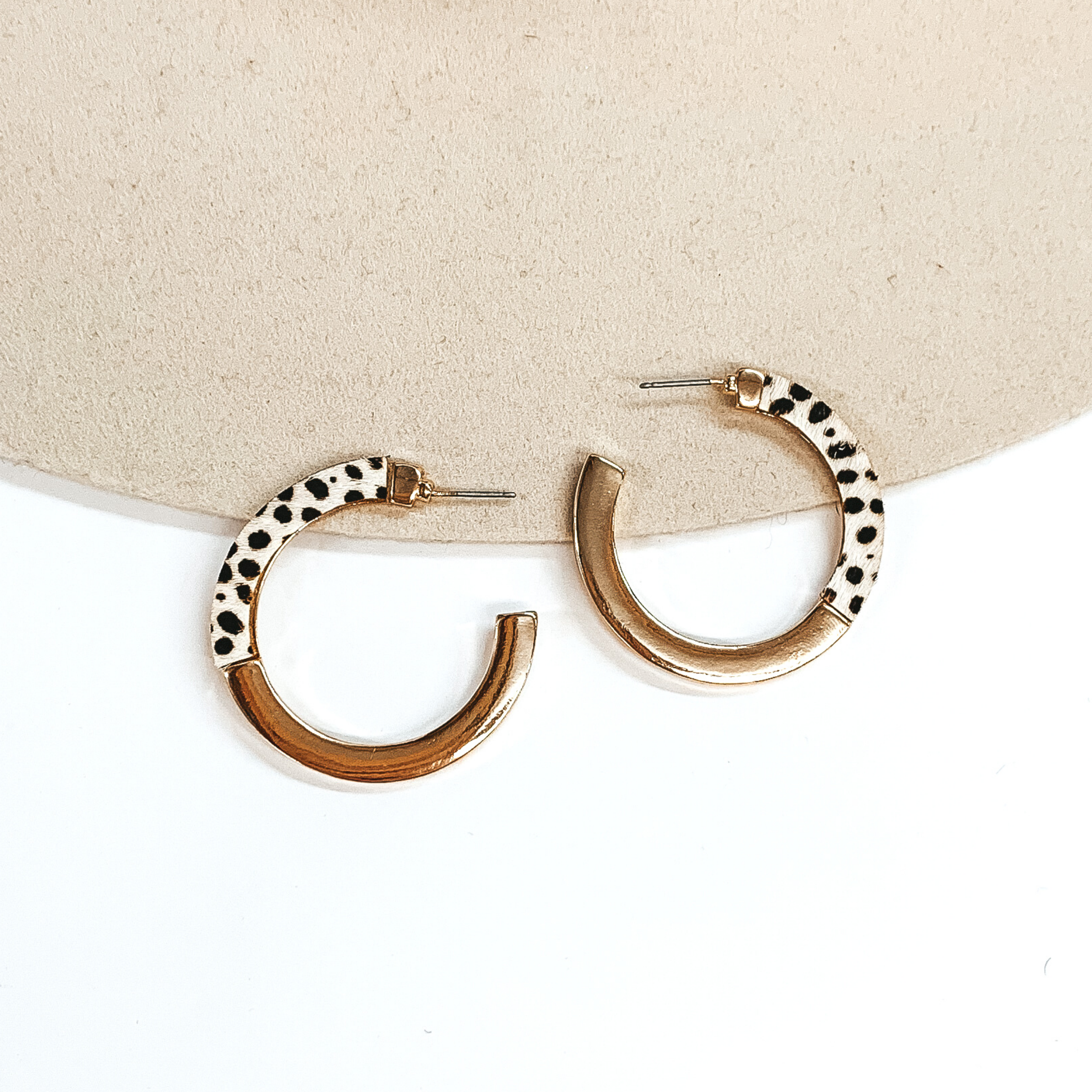 Flat hoops that are half gold and half ivory with a black cheetah print. These earrings are pictured on a white and beige background.