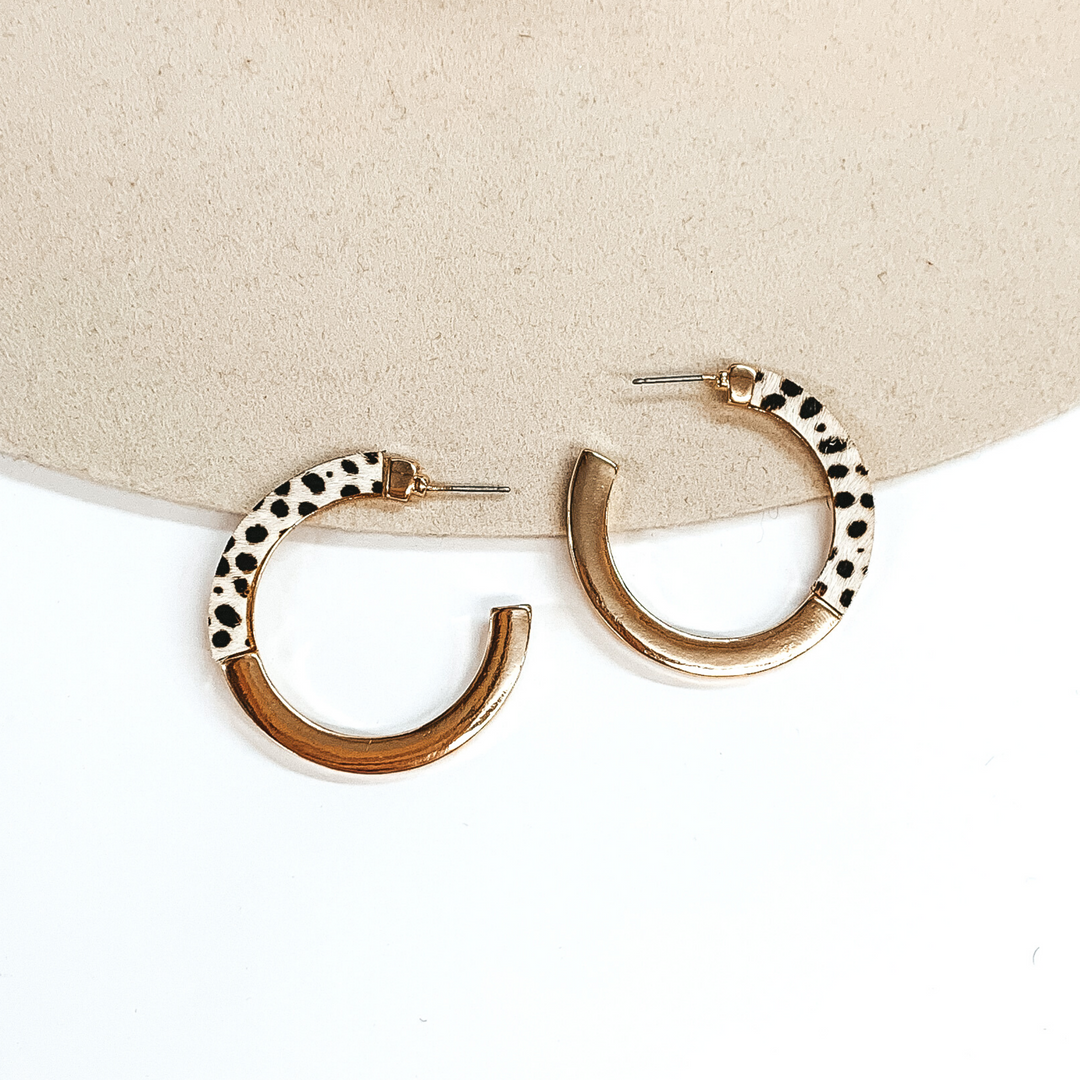 Flat hoops that are half gold and half ivory with a black cheetah print. These earrings are pictured on a white and beige background.