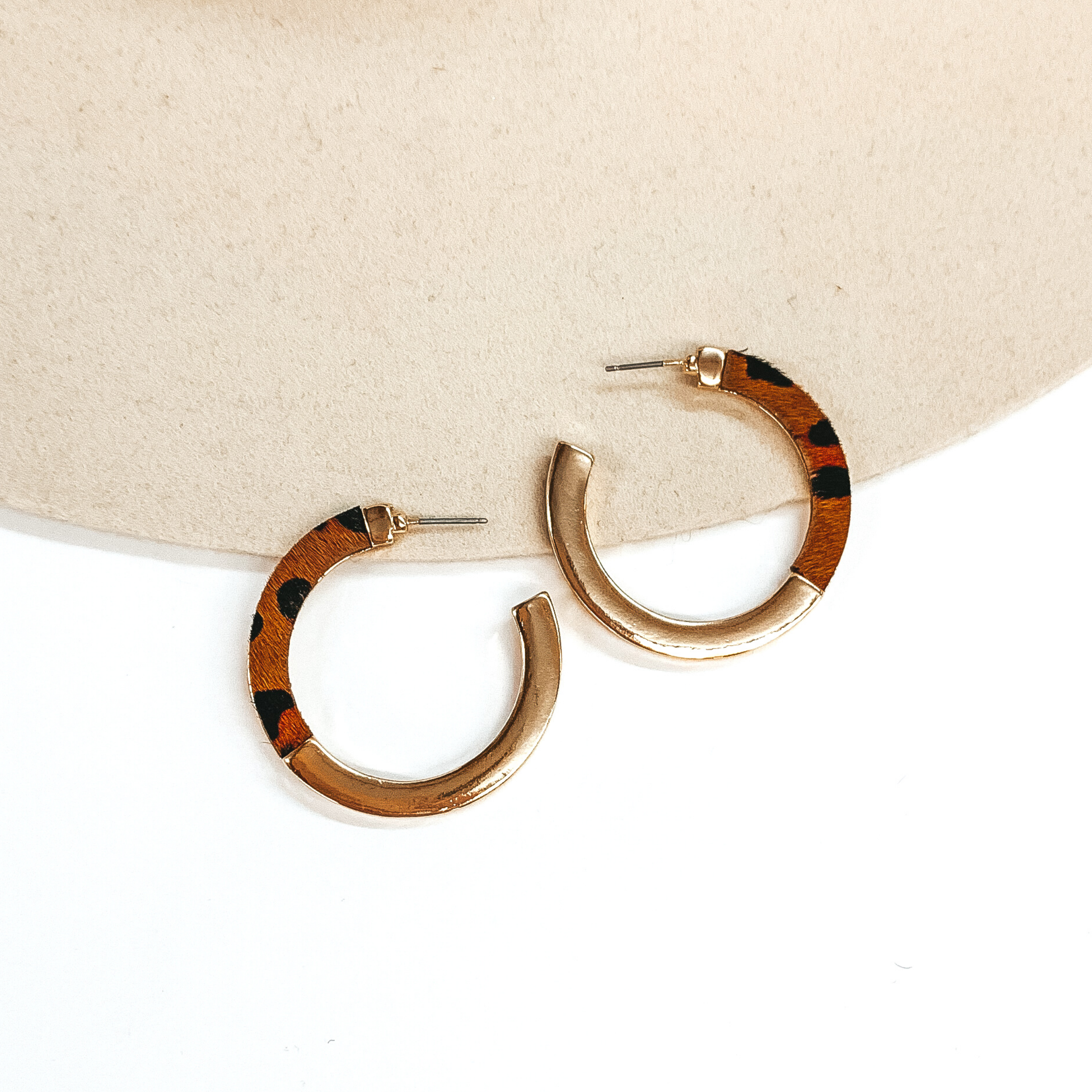  Flat hoops that are half gold and half brown with a black leopard print. These earrings are pictured on a white and beige background.