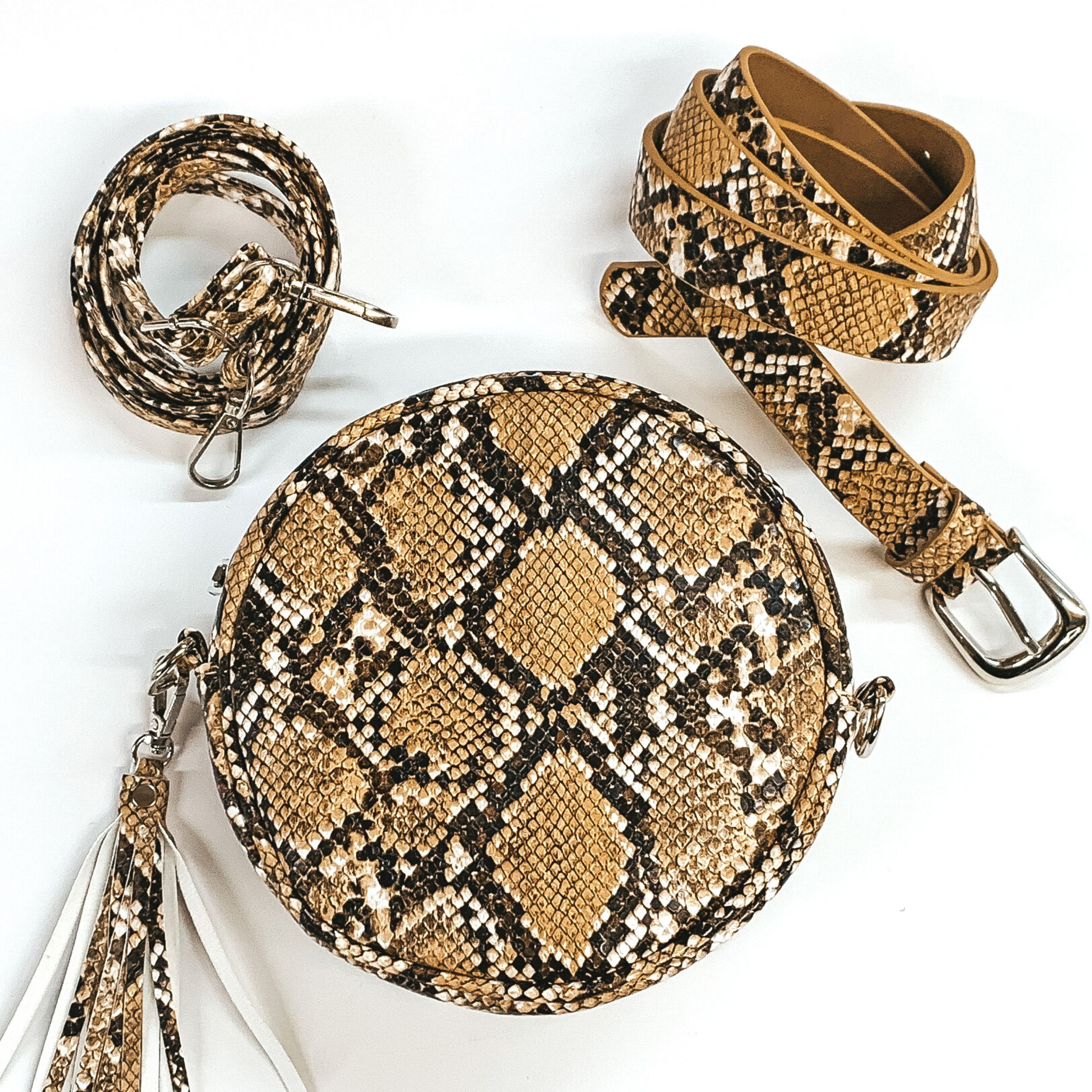 Black and brown snake print round purse with a snake print tassel pictured on a white background. At the top right of the picture there is a thick snake print strap with a silver buckle. At the top left corner there is a thin snake print strap with a silver hook on each end. 