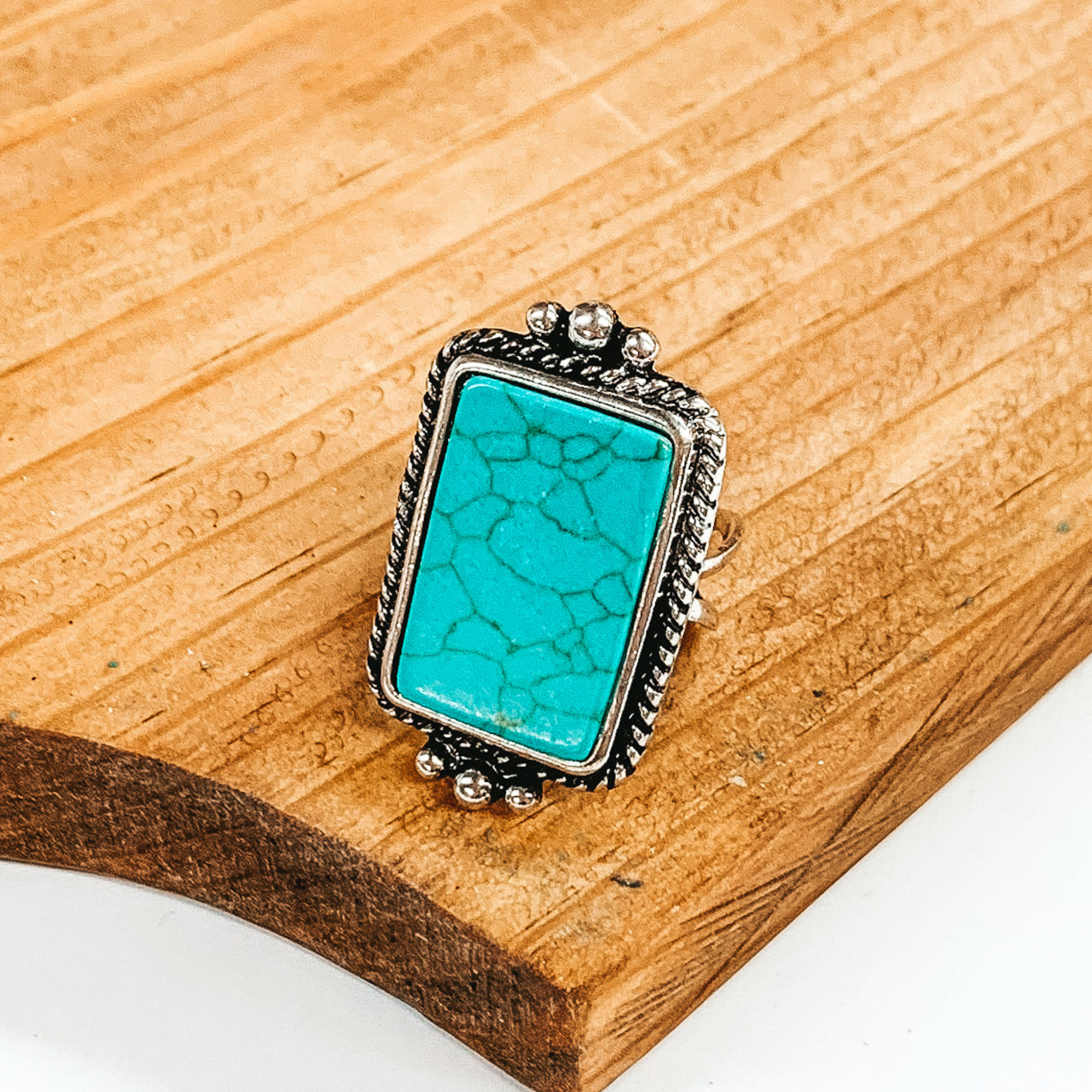  Silver cuff ring with reactangle, turquoise stone and silver detailed outline. This ring is pictured on a brown block on a white background. 