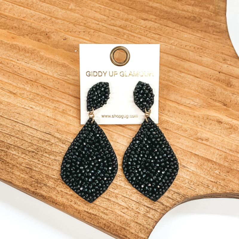 Black beaded teardrop earrings. These earrings are pictured on a brown block on a white background.