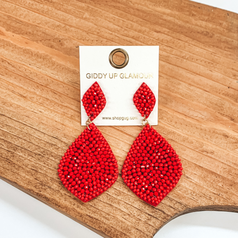 Red beaded teardrop earrings. These earrings are pictured on a brown block on a white background. 