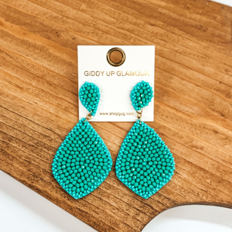 Turquoise beaded teardrop earrings. These earrings are pictured on a brown block on a white background.