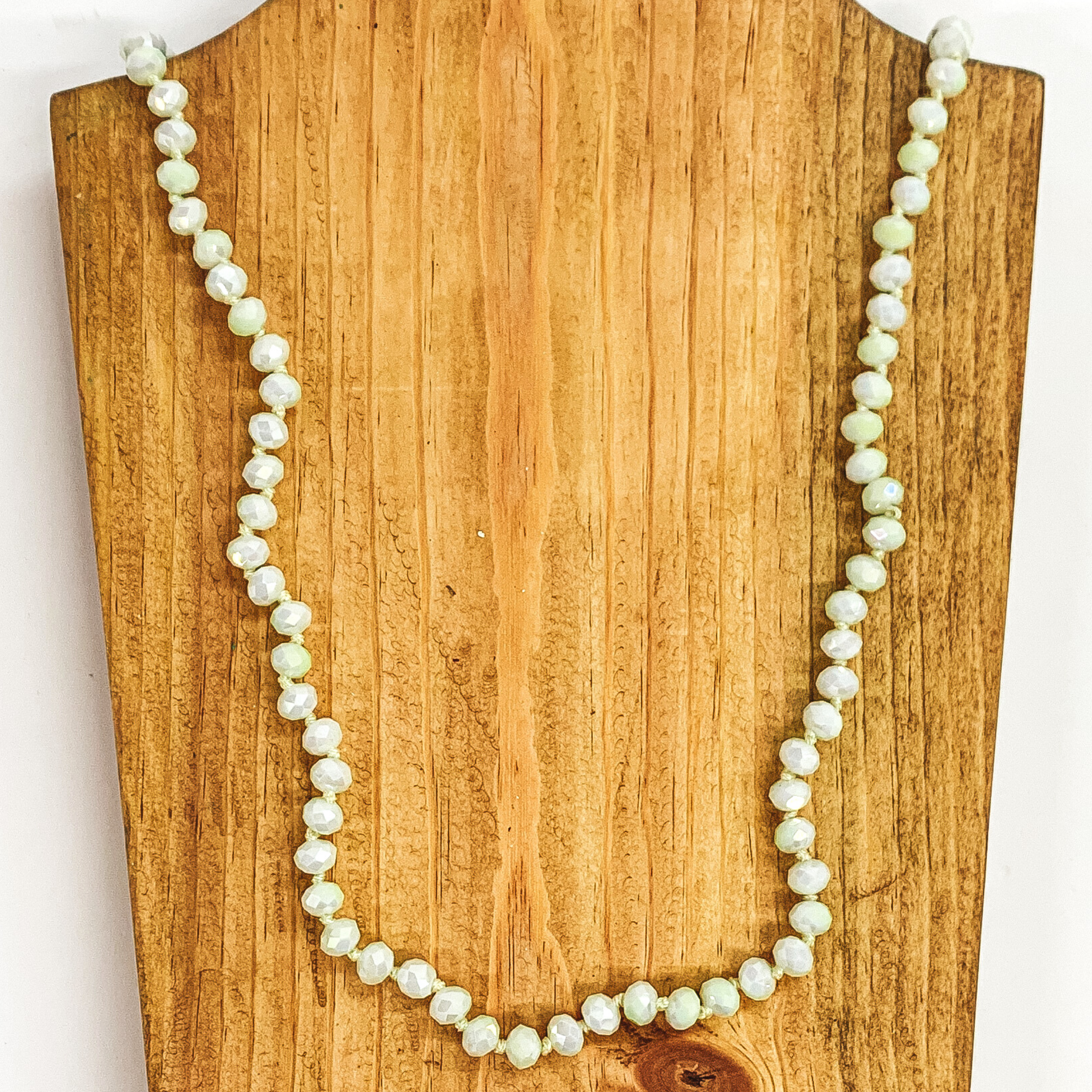 Lime sherbert crystal beaded necklace. This necklace is pictured on a brown block on a white background. 