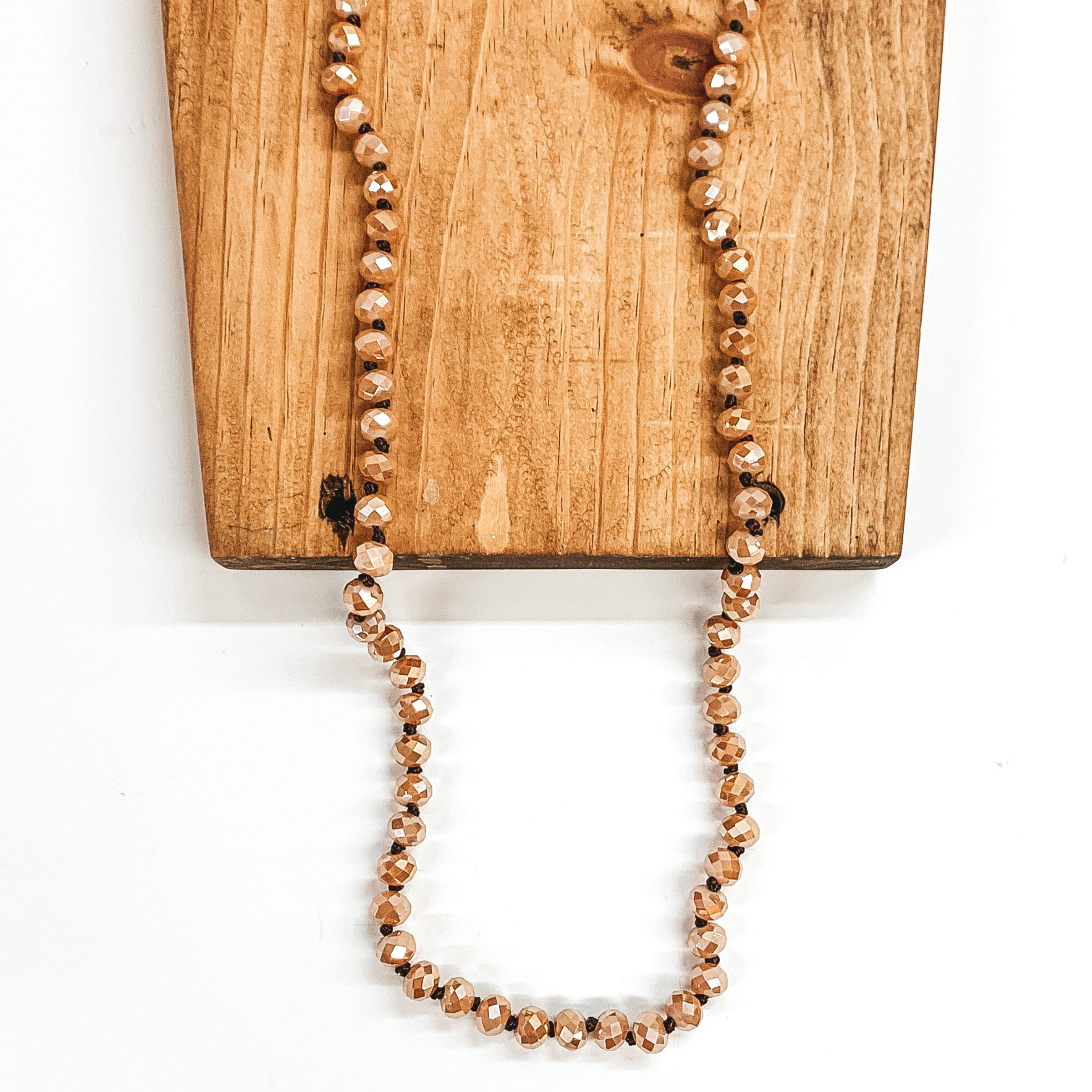 Latte crystal beaded necklace. This necklace is pictured on a brown block on a white background.