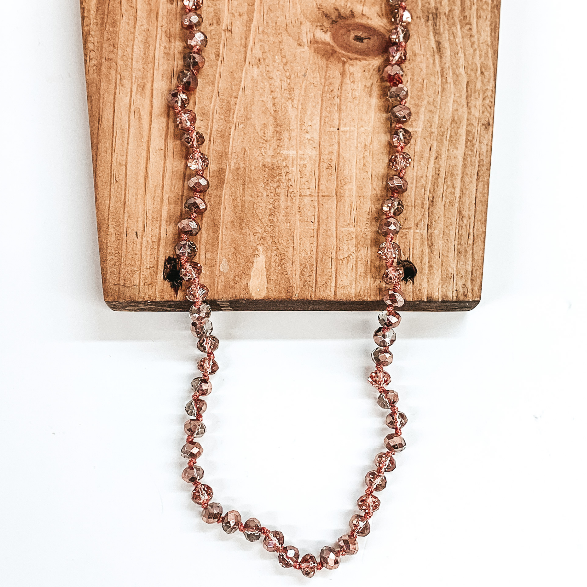 Rose gold and clear mix crystal beaded necklace. This necklace is pictured on a brown block on a white background.