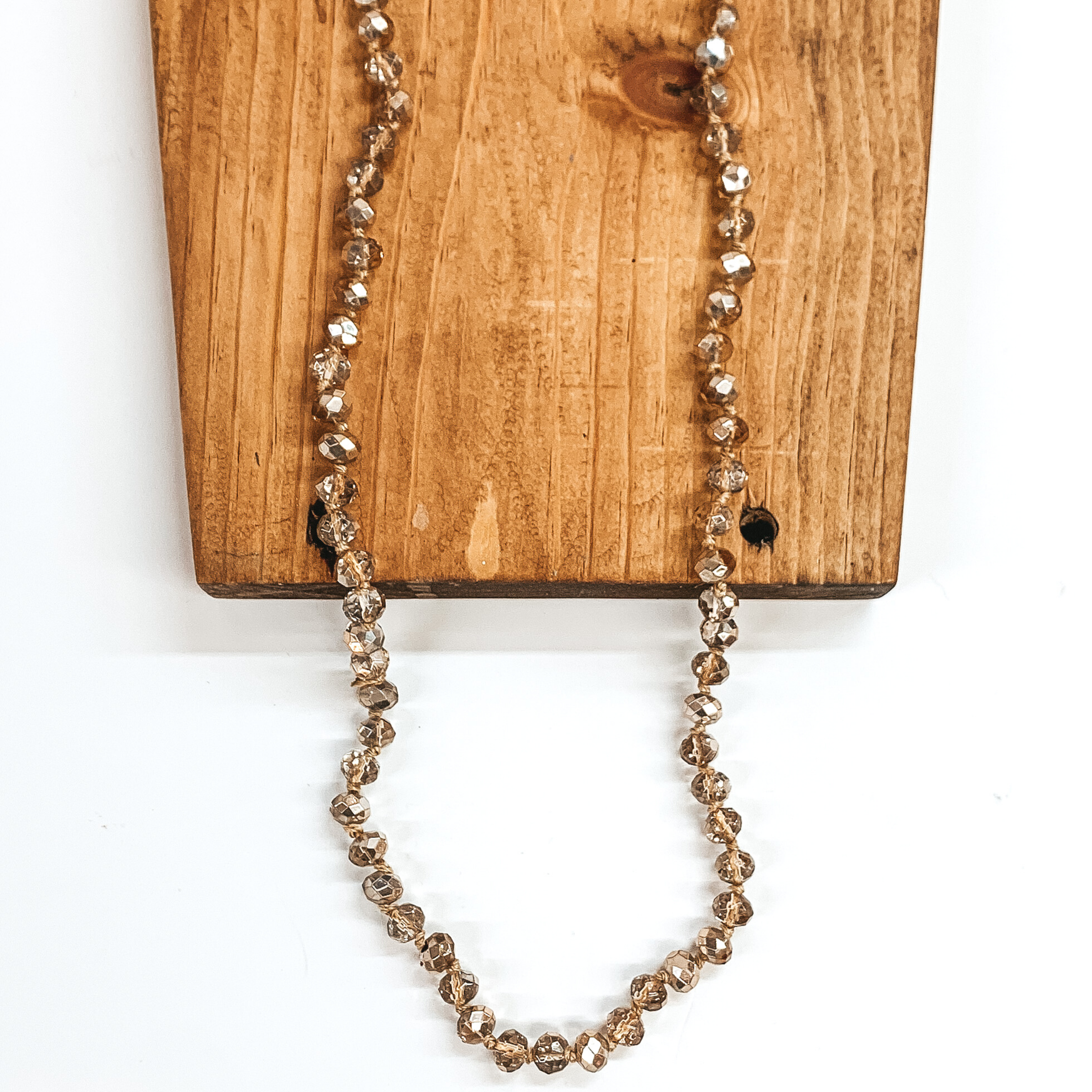Gold and clear mix crystal beaded necklace. This necklace is pictured on a brown block on a white background.