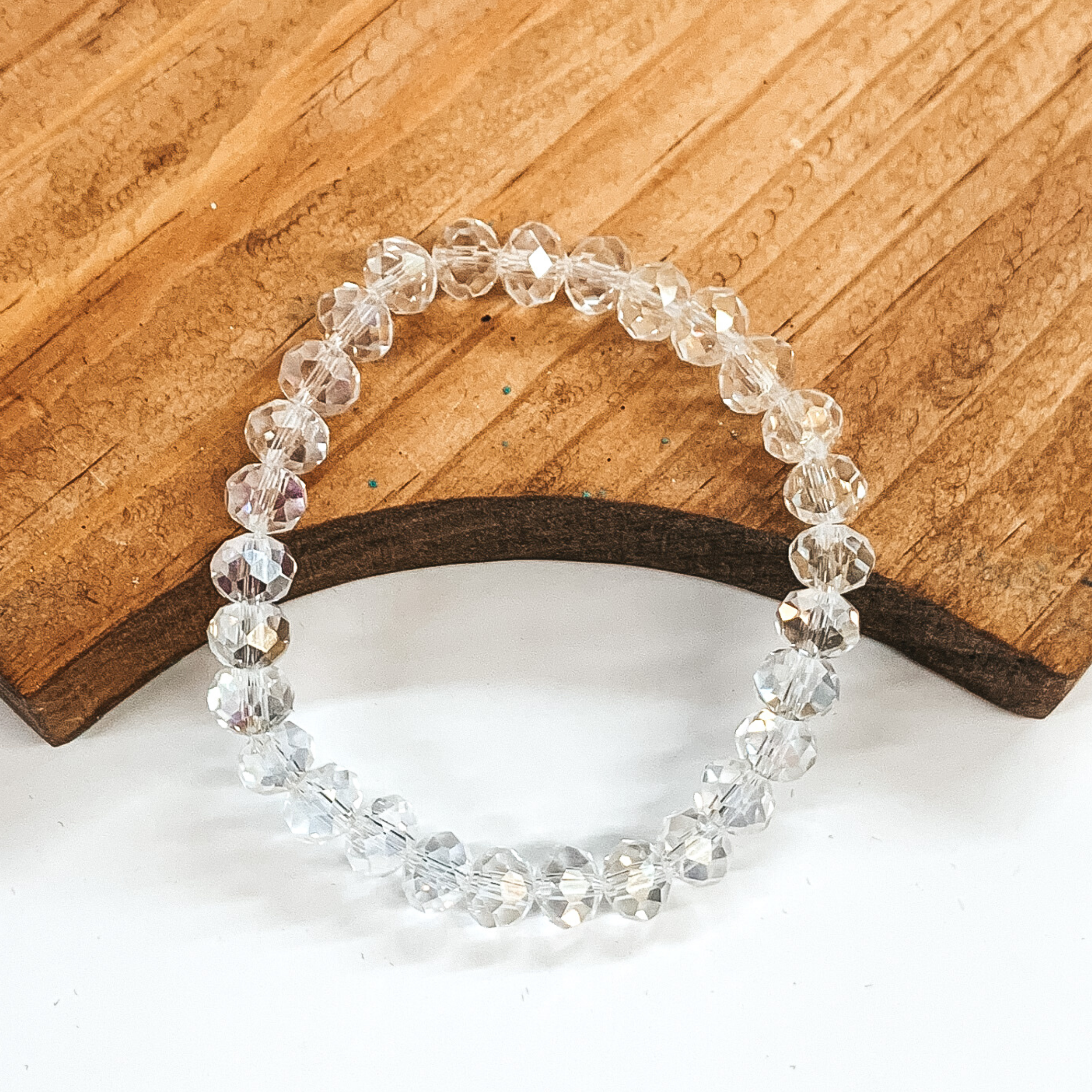 Clear AB crystal beaded bracelet. This bracelet is pictured laying partially on a brown block on a white background. 