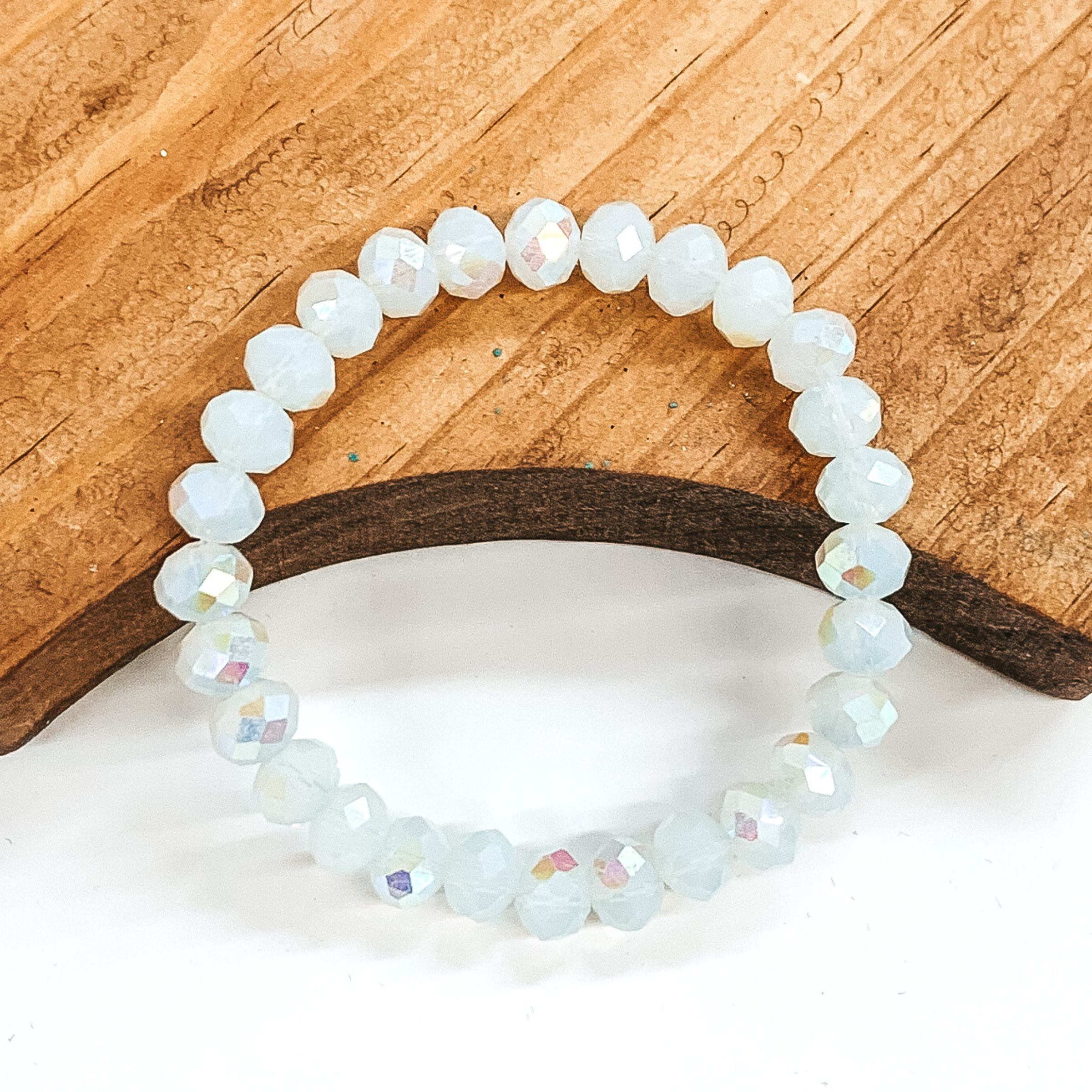 White AB crystal beaded bracelet. This bracelet is pictured laying partially on a brown block on a white background.