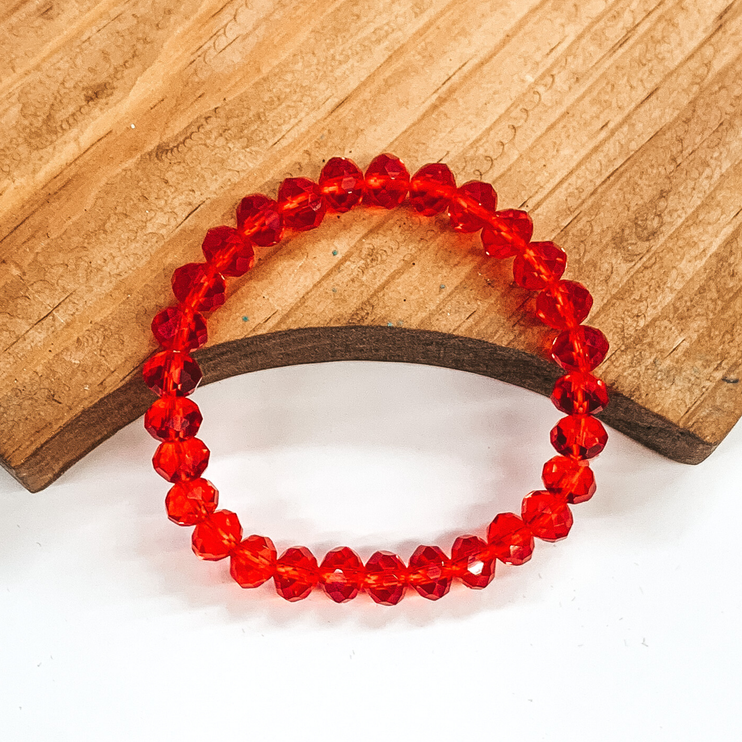 Red crystal beaded bracelet. This bracelet is pictured laying partially on a brown block on a white background.