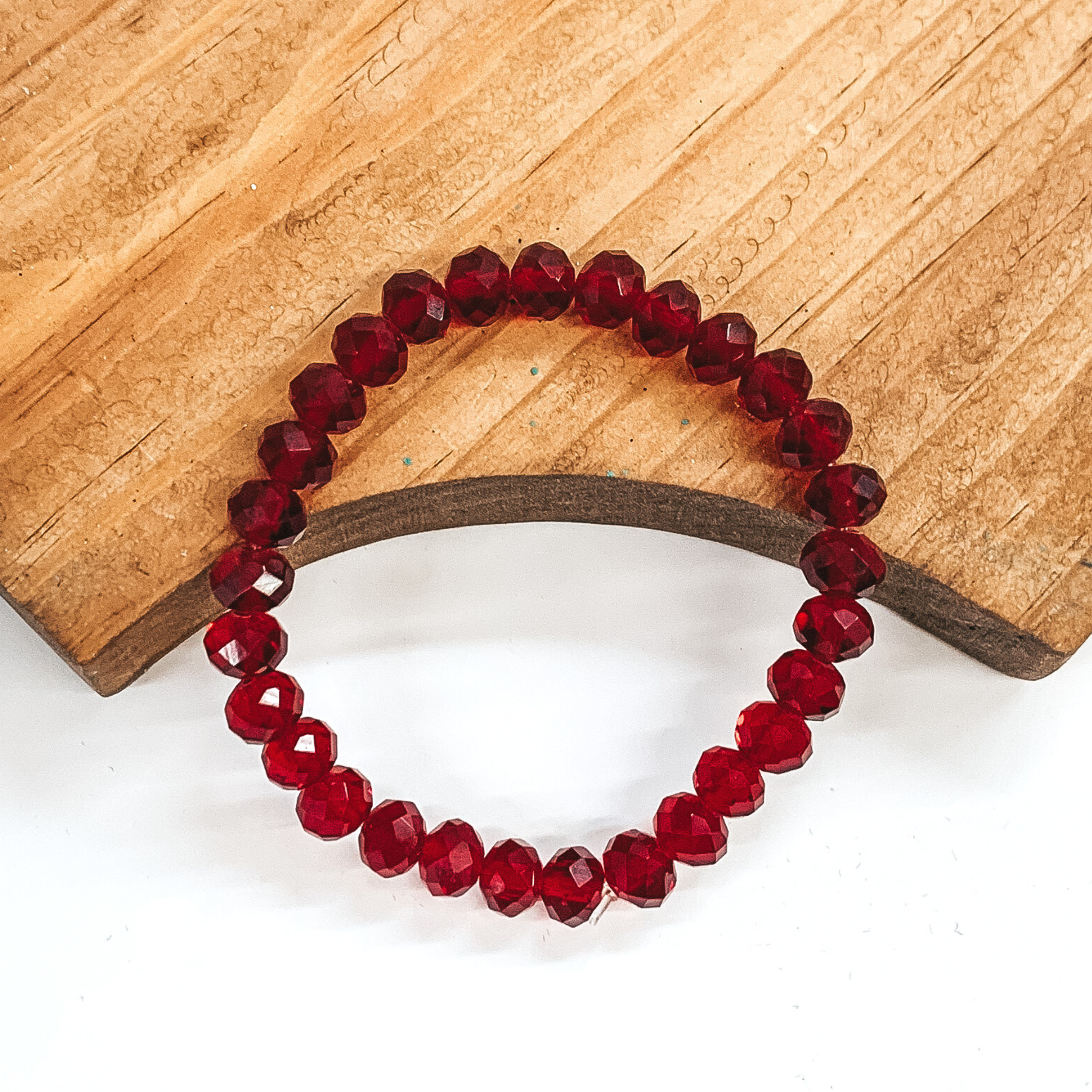 Maroon crystal beaded bracelet. This bracelet is pictured laying partially on a brown block on a white background.