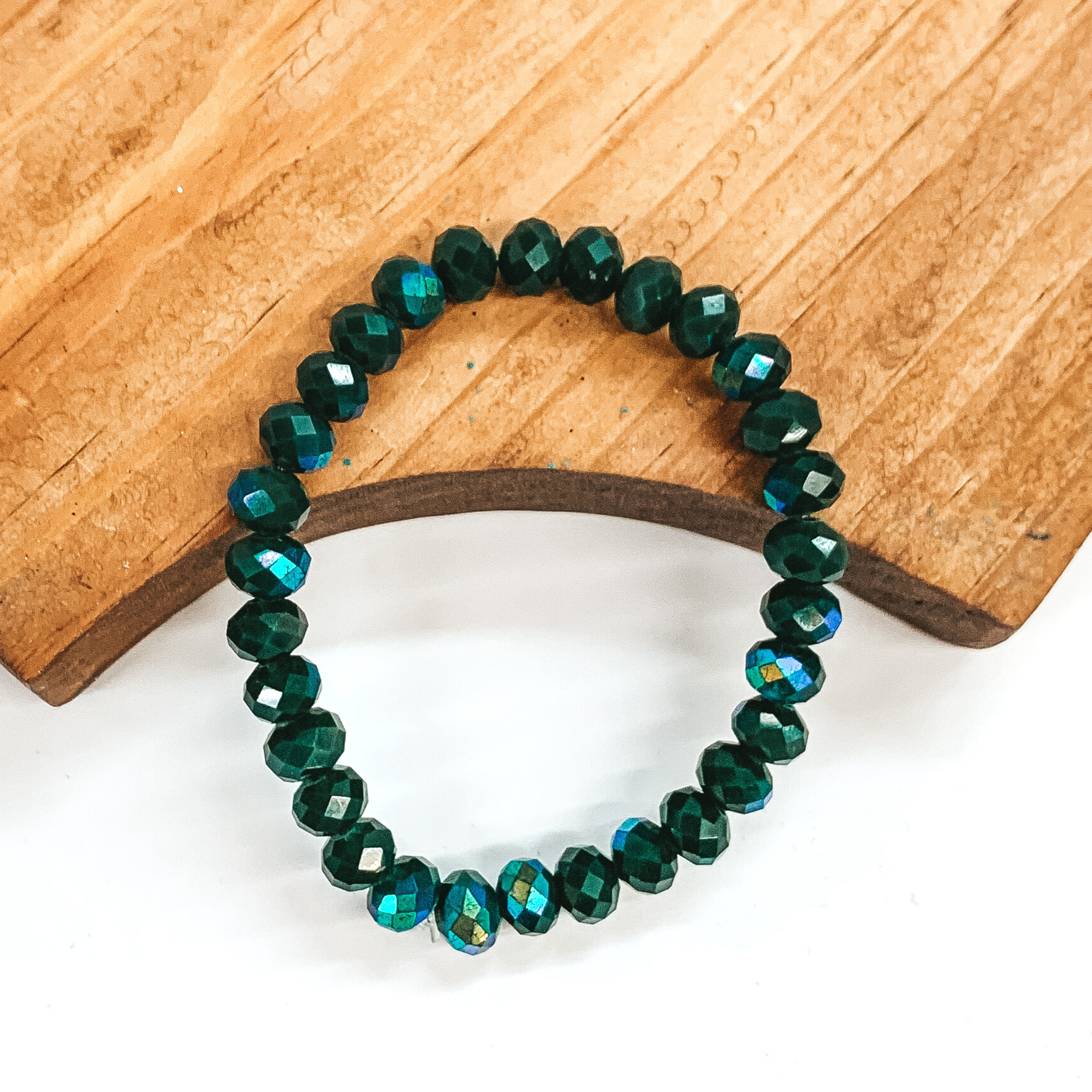 Hunter green AB crystal beaded bracelet. This bracelet is pictured laying partially on a brown block on a white background.