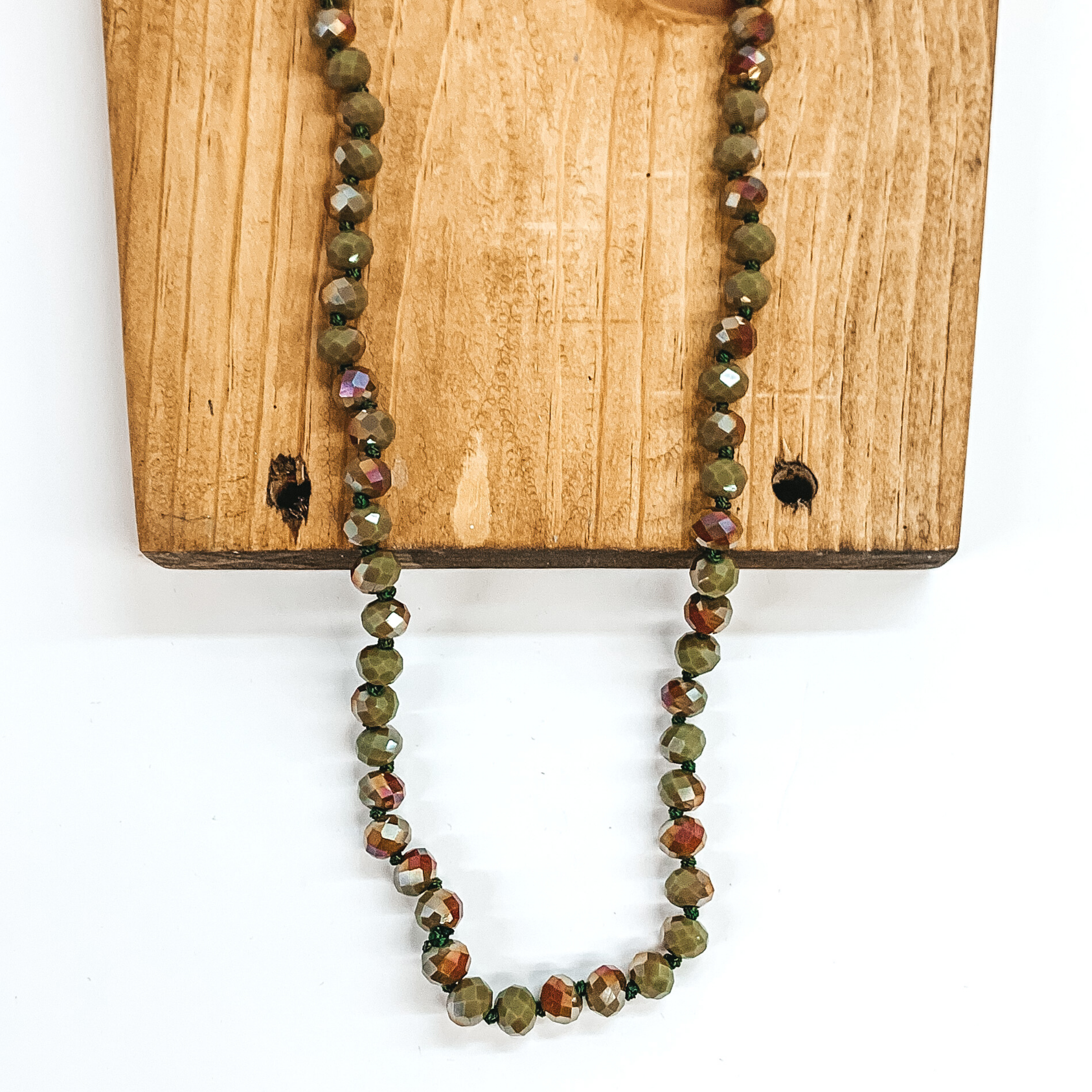 Camo green crystal beaded necklace. This necklace is pictured on a brown block on a white background. This necklace is laying on top of a brown block on a white background.