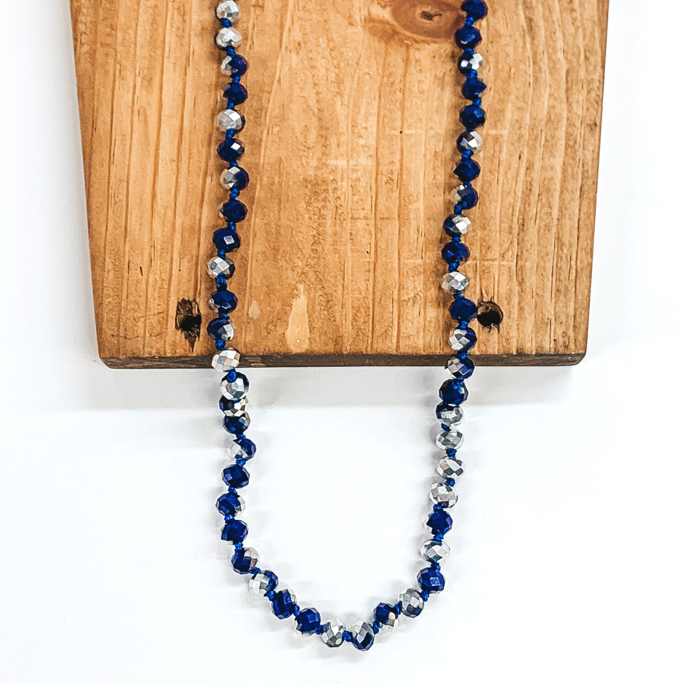 Blue and silver crystal beaded necklace. This necklace is laying on top of a brown block on a white background.