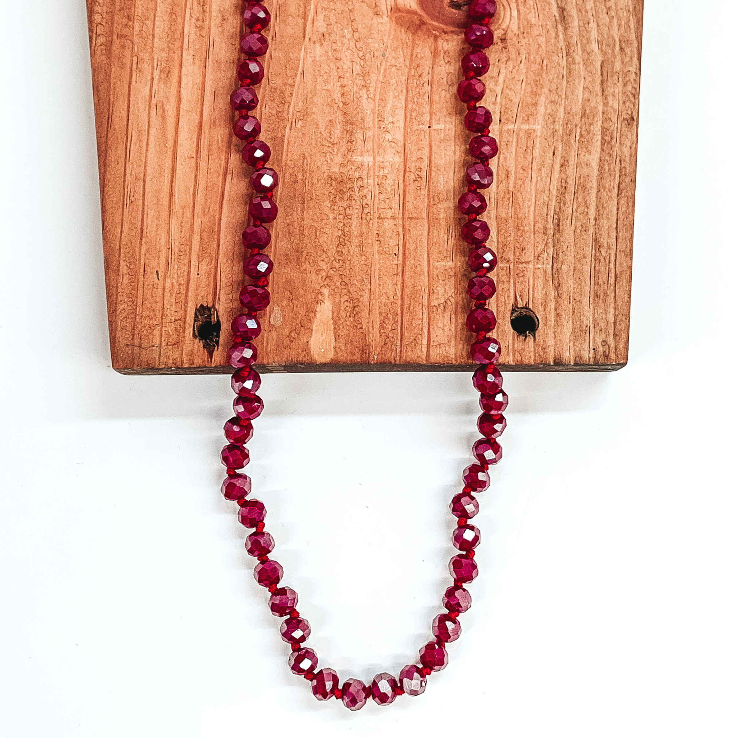 Garnet AB crystal beaded necklace. This necklace is laying on top of a brown block on a white background.