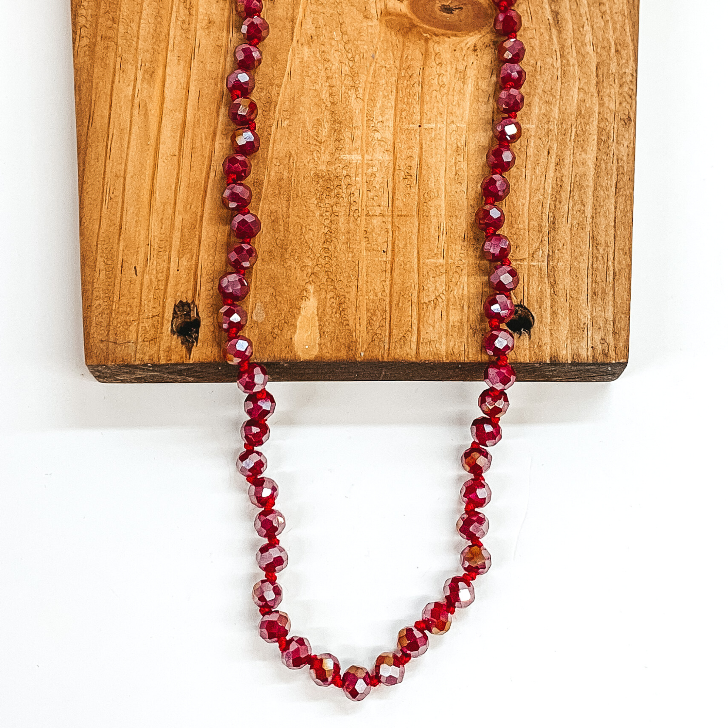 Red AB crystal beaded necklace. This necklace is laying on top of a brown block on a white background.